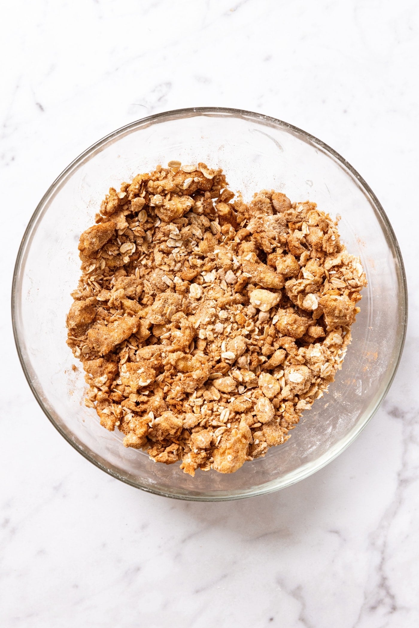 Glass bowl on white marble surface with mixed streusel topping before being placed on crisp.