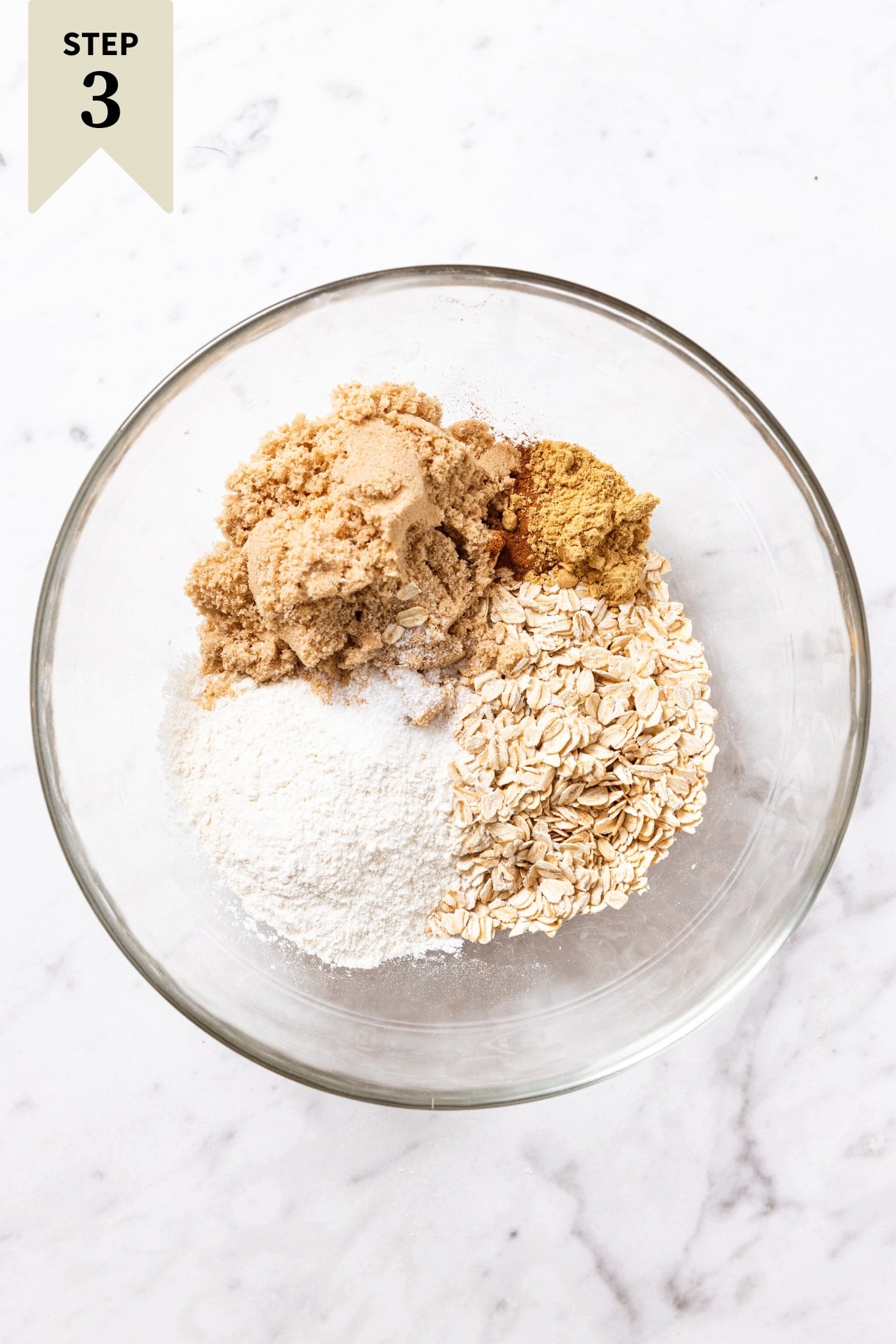 Glass bowl filled with the ingredients needed to make a streusel topping including brown sugar, oats, spices, and flour.