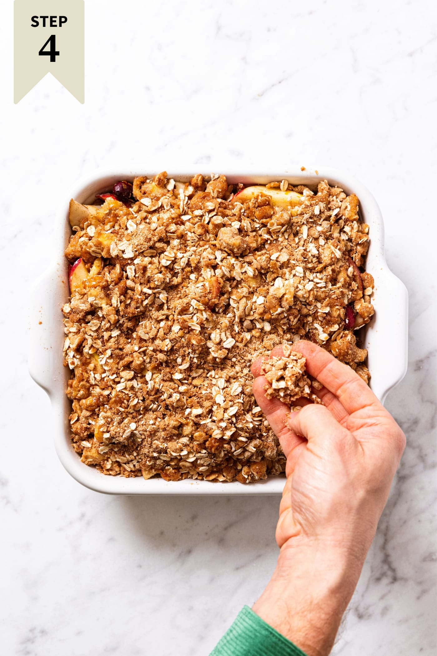 White baking dish filled with cranberry crisp with hand sprinkled streusel topping all over the top before being baked in the oven.