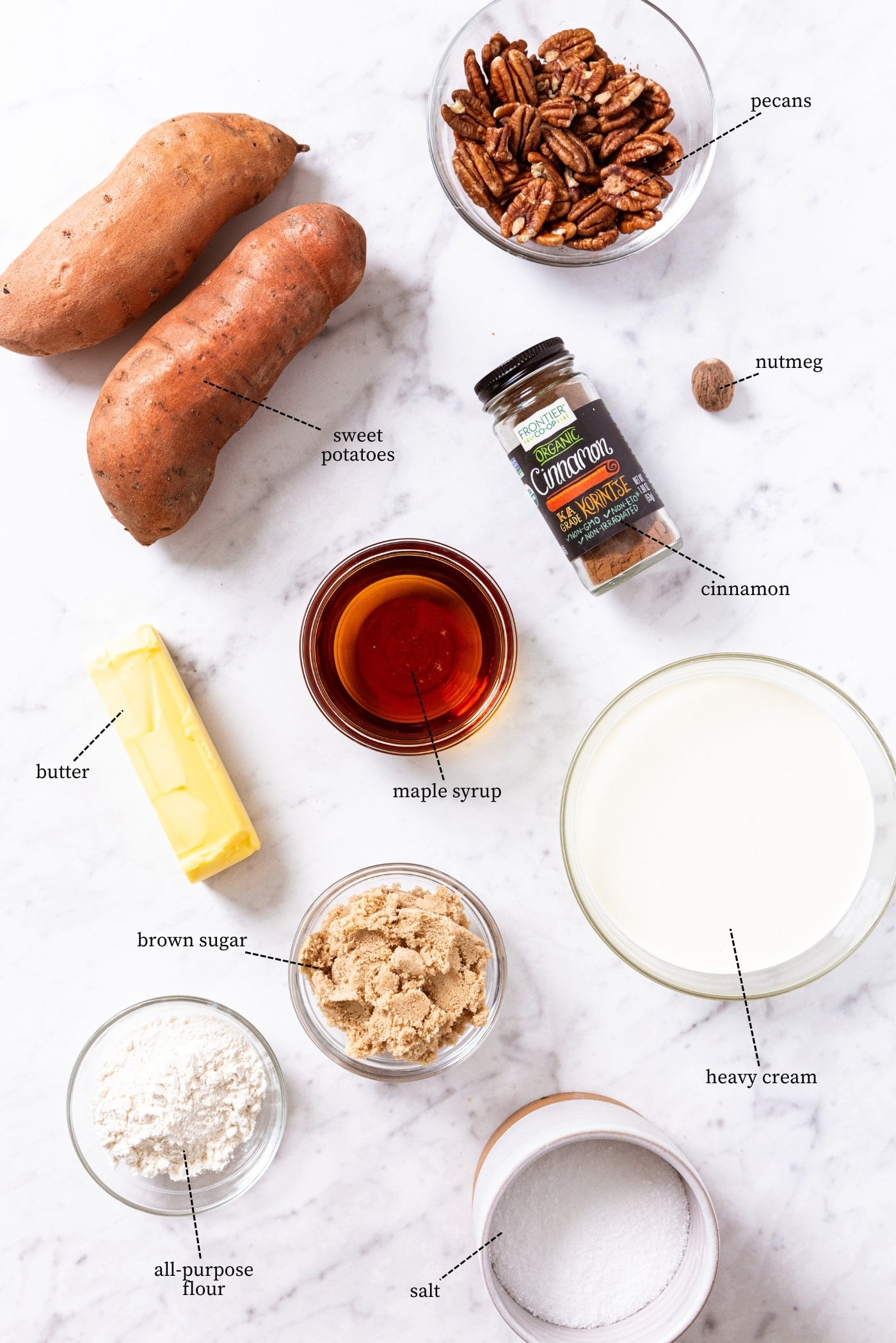 White marble piece with all ingredients needed to make sweet potato casserole including sweet potatoes, pecans, maple syrup, butter, spices, and more.