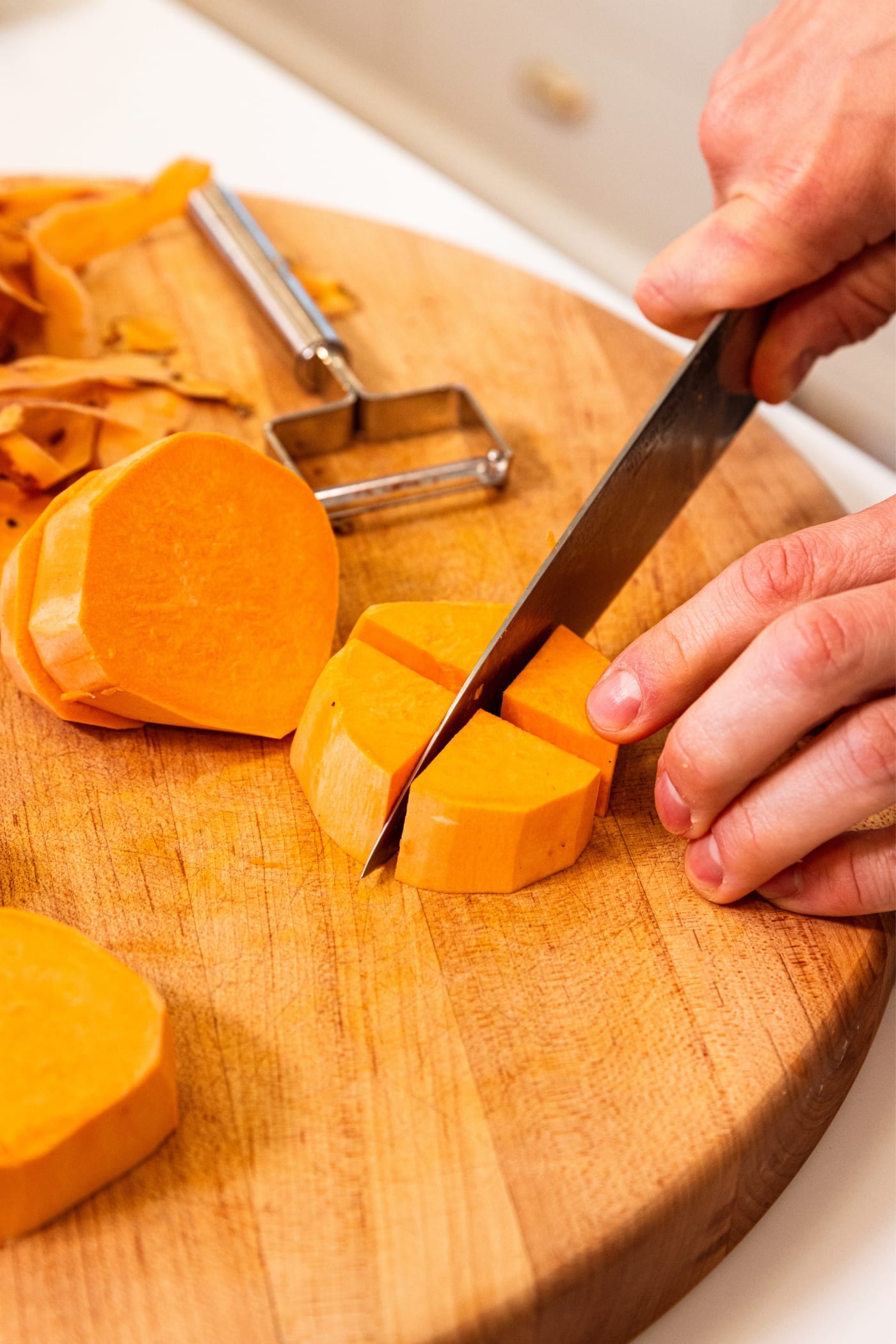 Hand holding onto slice of sweet potato after slicing it into quarters on a wood cutting board with more of the sweet potato to the side.