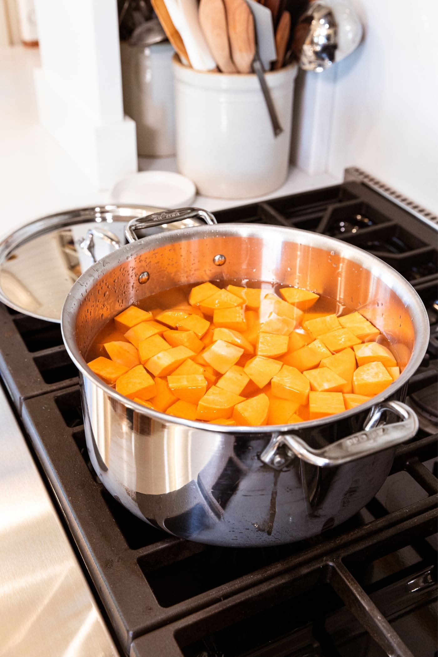 Large metal stockpot sitting on stovetop filled with water and chunks of orange colored sweet potatoes before being cooked.
