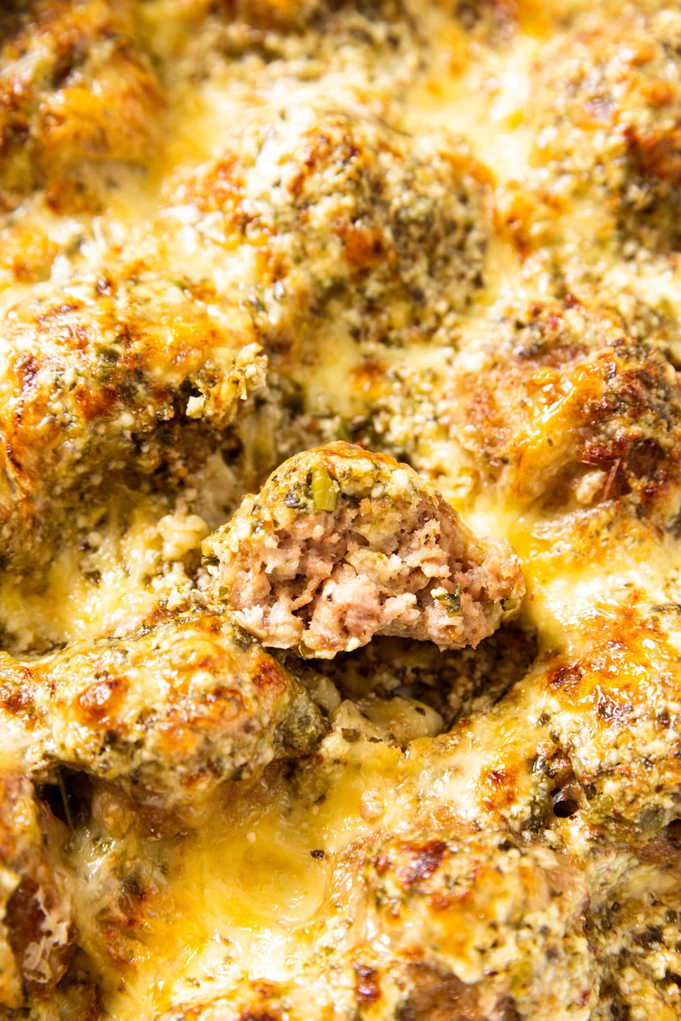 Baked meatballs with cheese sprinkled all over the top with one meatball cut in half showing soft interior texture.