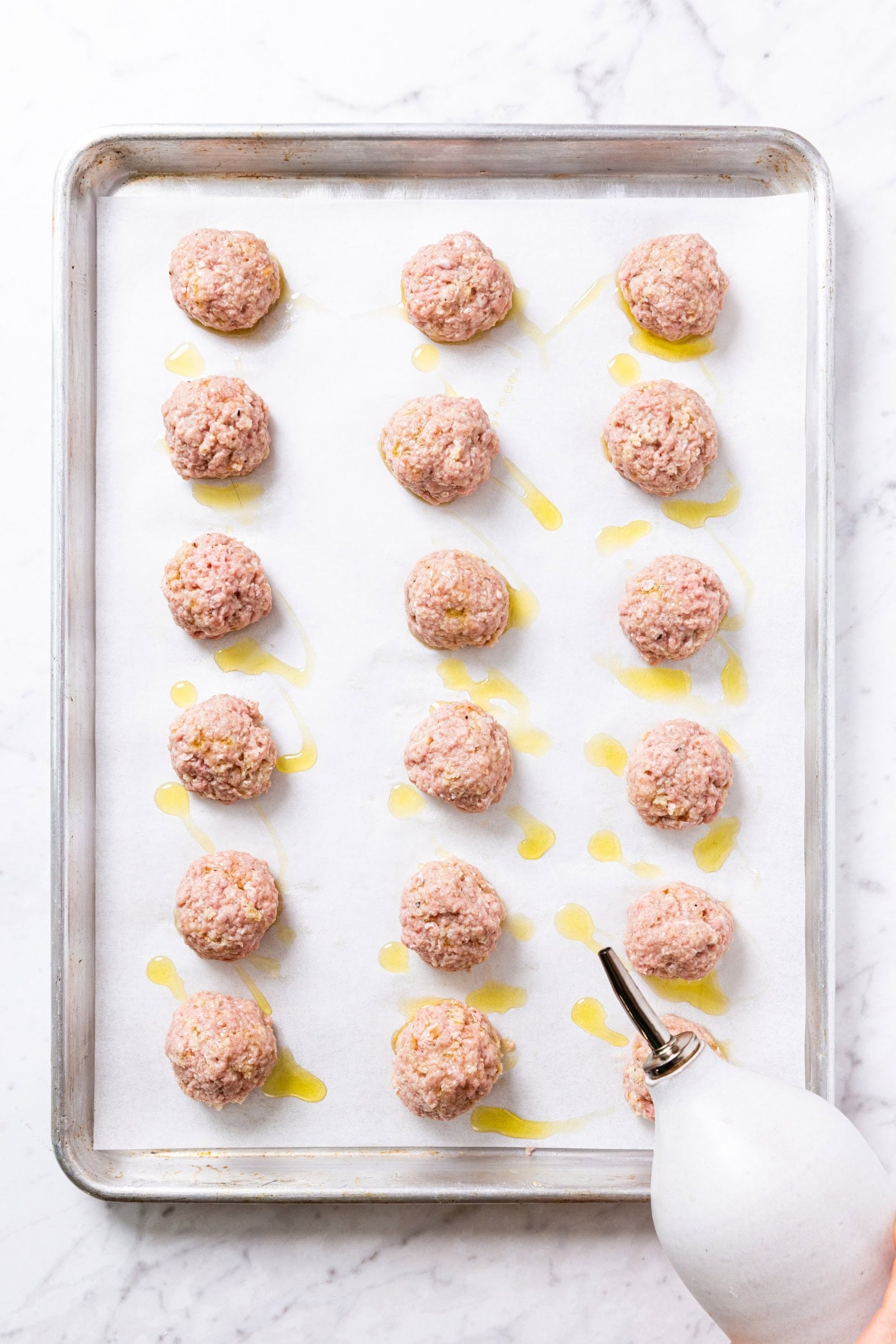 Metal baking sheet with raw meatballs using a container to sprinkle
