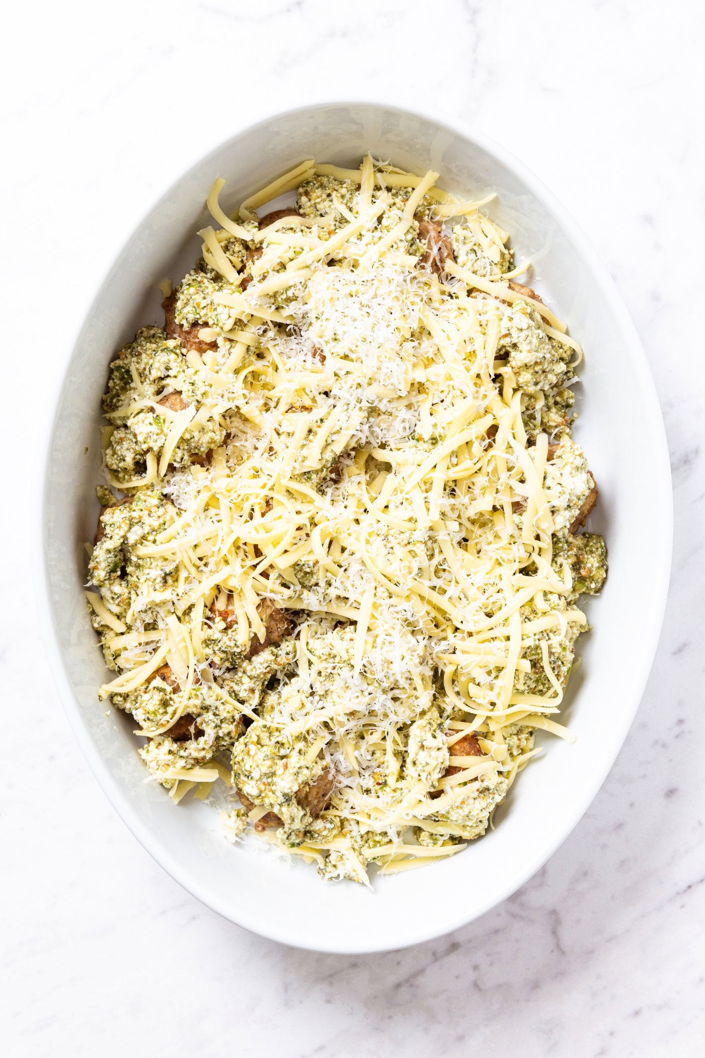 Unbaked meatballs topped with Parmesan cheese in oval baking dish right before going in the oven to bake sitting on marble surface.