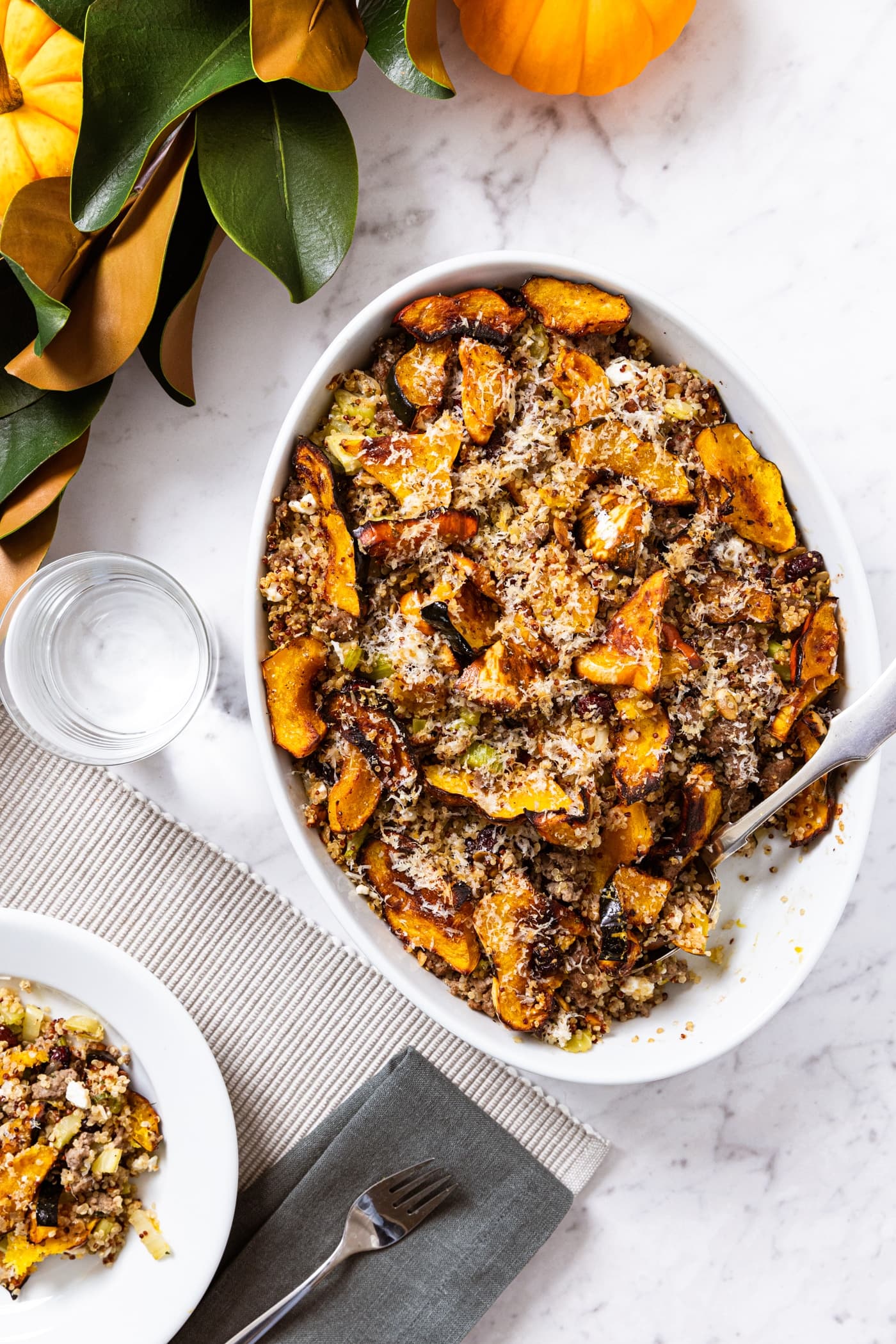 White marble surface with white baking dish filled with stuffed acorn squash casserole with spoon resting in dish along with magnolia garland.
