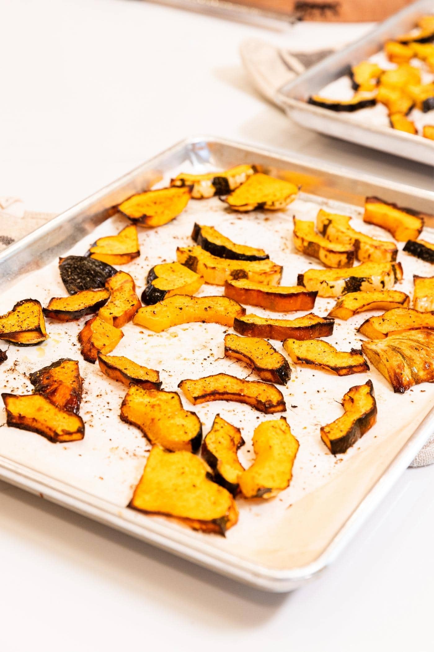 Roasted pieces of acorn squash with browned edges sitting on parchment-lined baking sheet on white countertop after coming out of the oven.