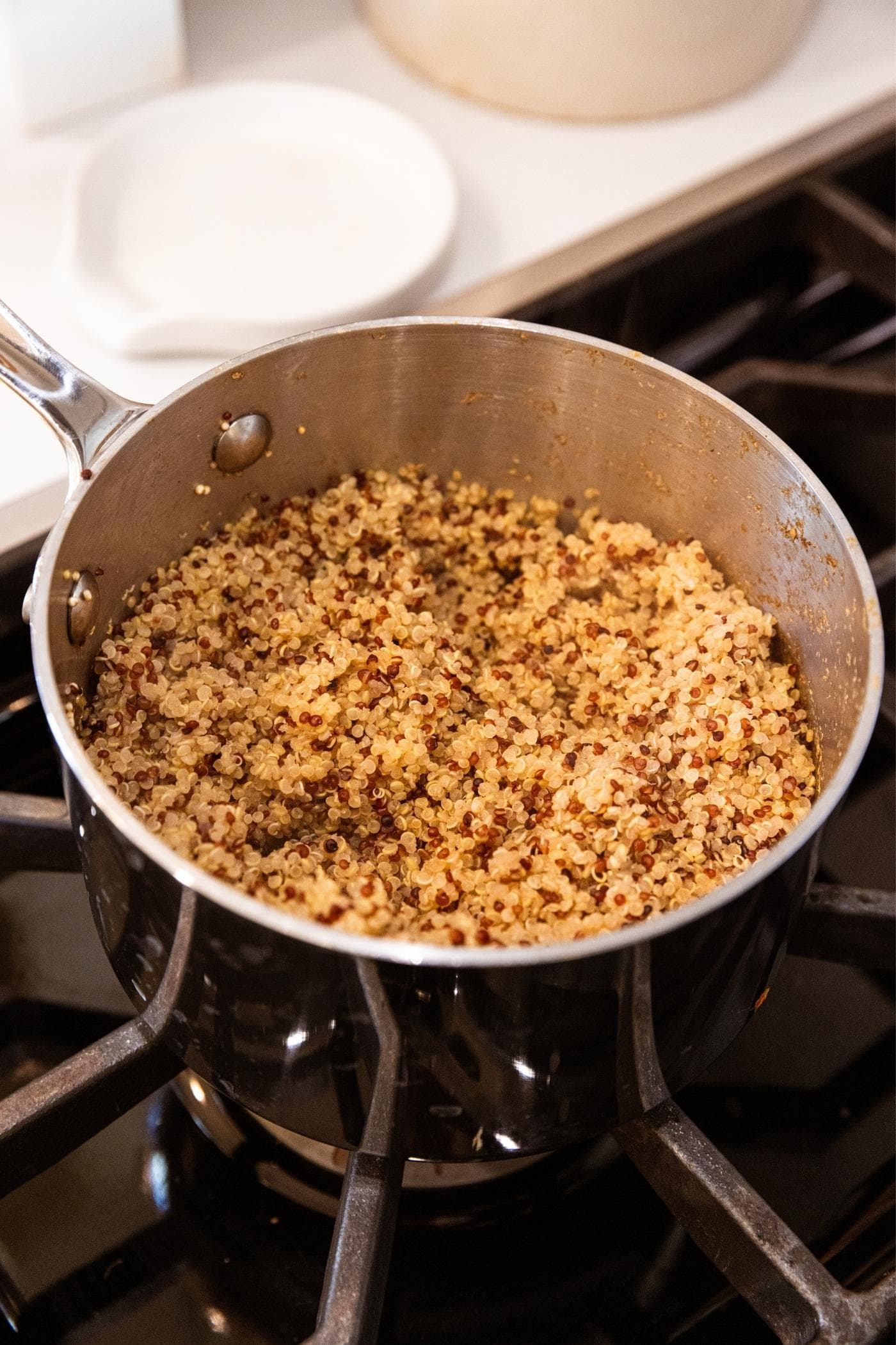 Fully cooked quinoa sitting in metal kettle on stovetop after cooking.