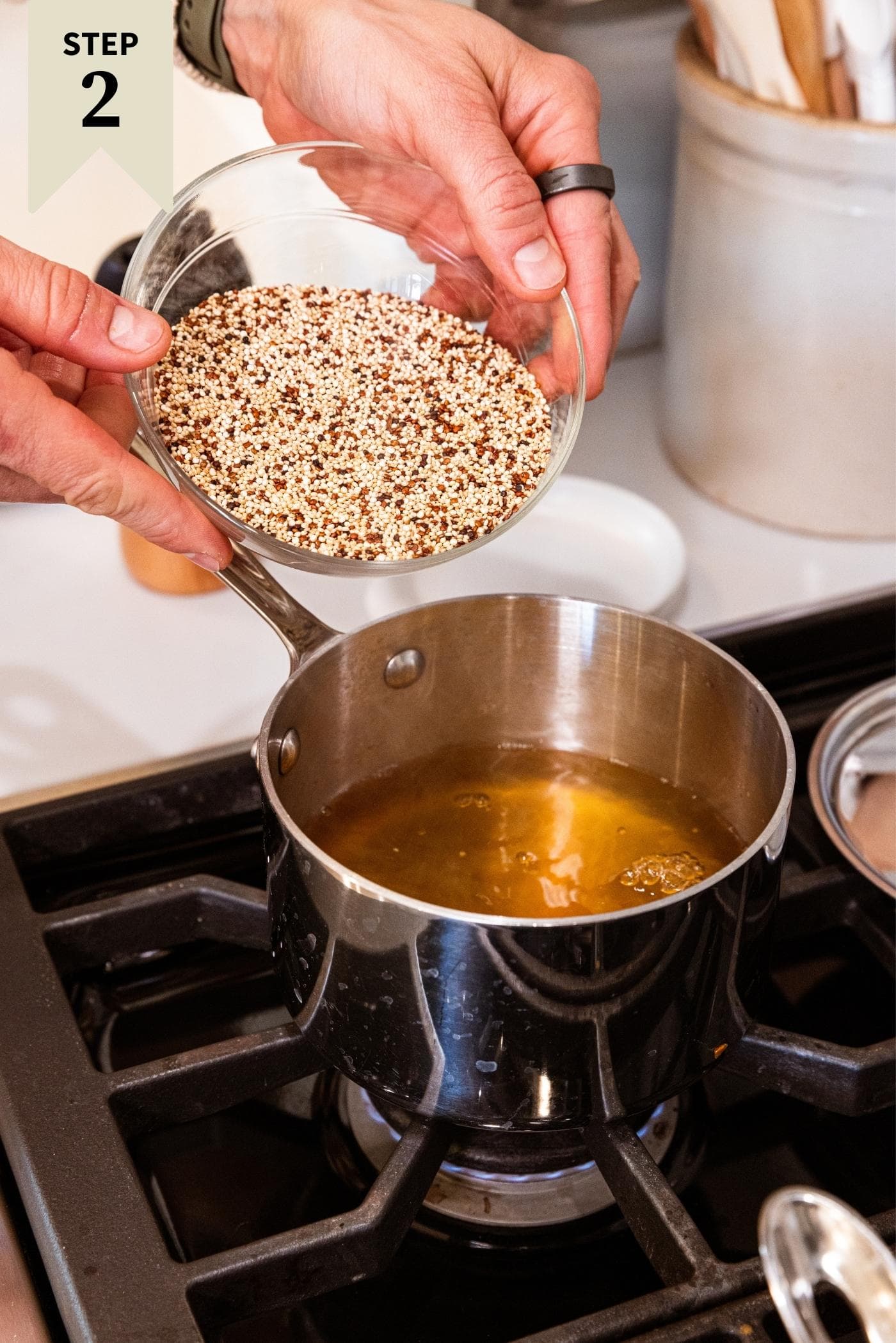 Kettle with vegetable stock inside with two hands about to pour quinoa into kettle on stovetop.
