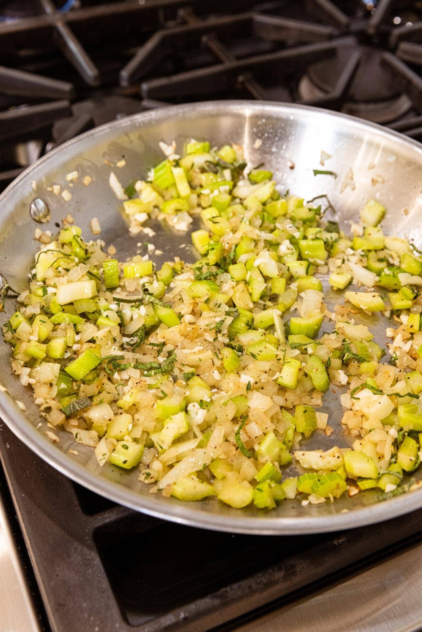 Metal skillet with cooked celery and onion and herbs after cooking in oil on stovetop.