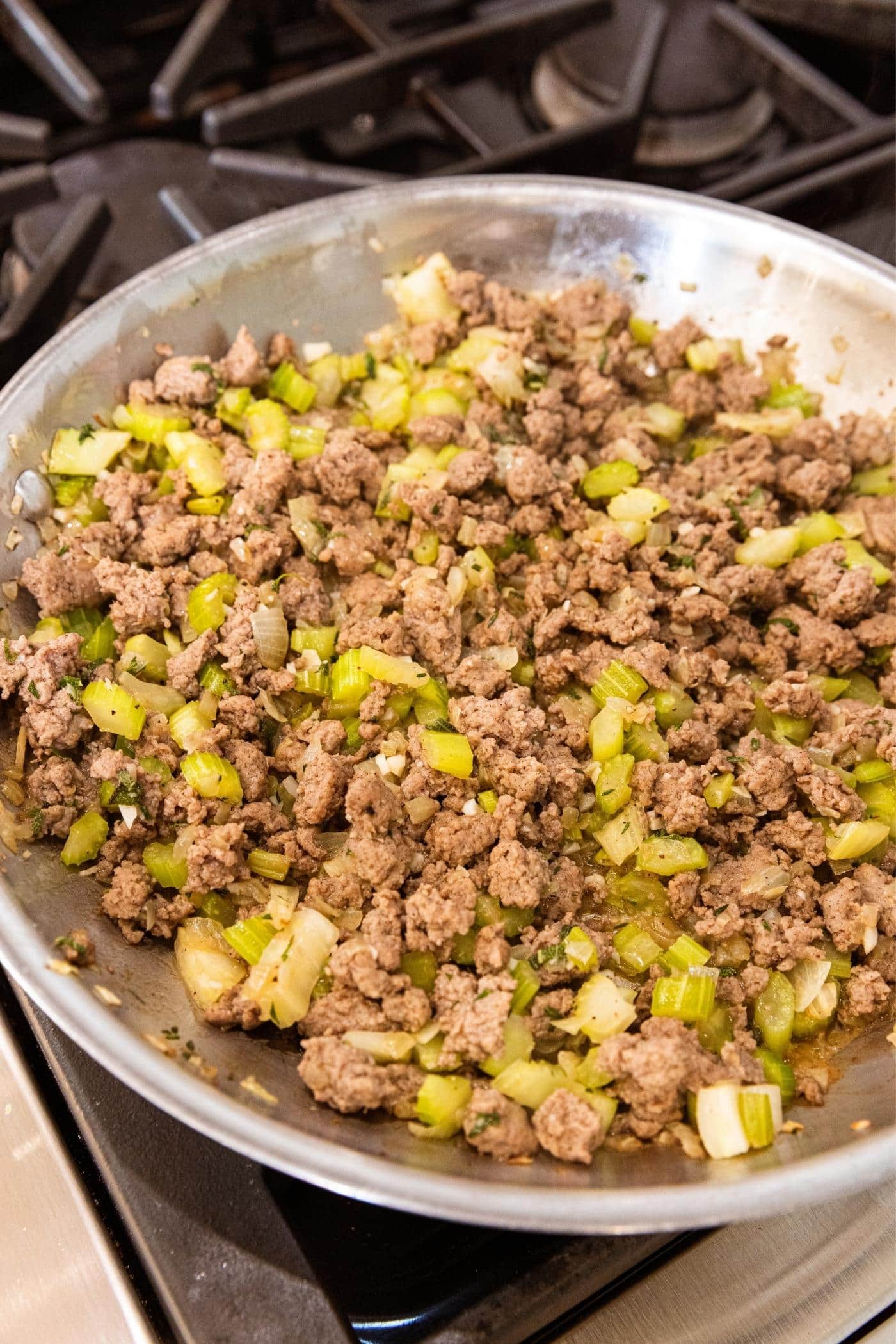 Metal skillet filled with mixture of cooked ground sausage along with diced onion and celery and herbs all browned.