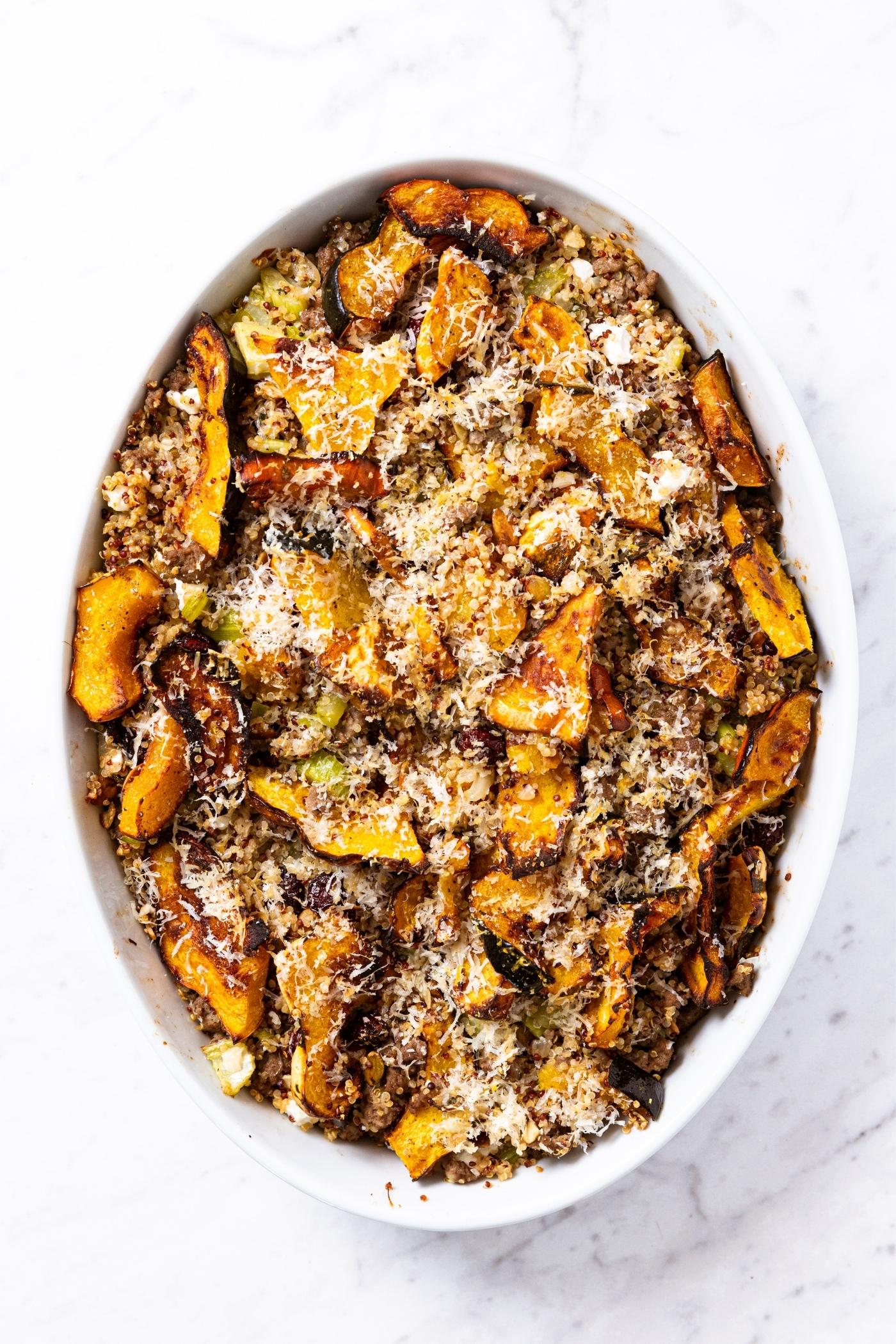 White baking dish filled with baked acorn squash casserole mixture sitting on white marble surface right after coming out of the oven.
