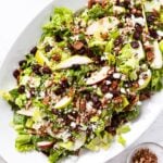 White platter sitting on marble surface filled with lettuce wild rice salad topped with dried cranberries and pears as well as feta cheese.