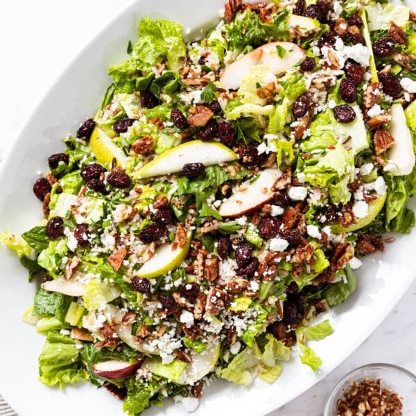 White platter sitting on marble surface filled with lettuce wild rice salad topped with dried cranberries and pears as well as feta cheese.