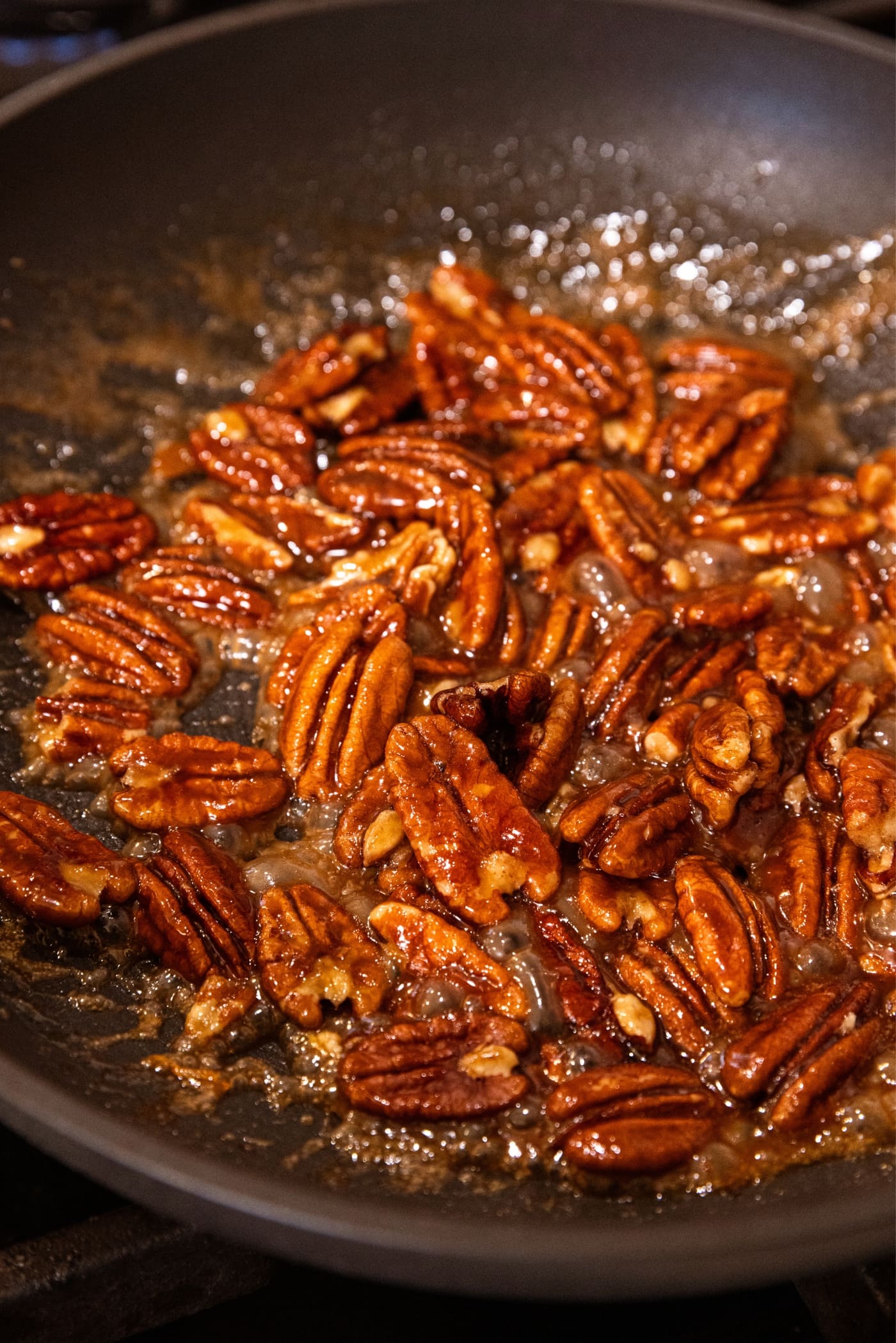 Small black skillet filled with candied praline pecans with gooey liquid all around.