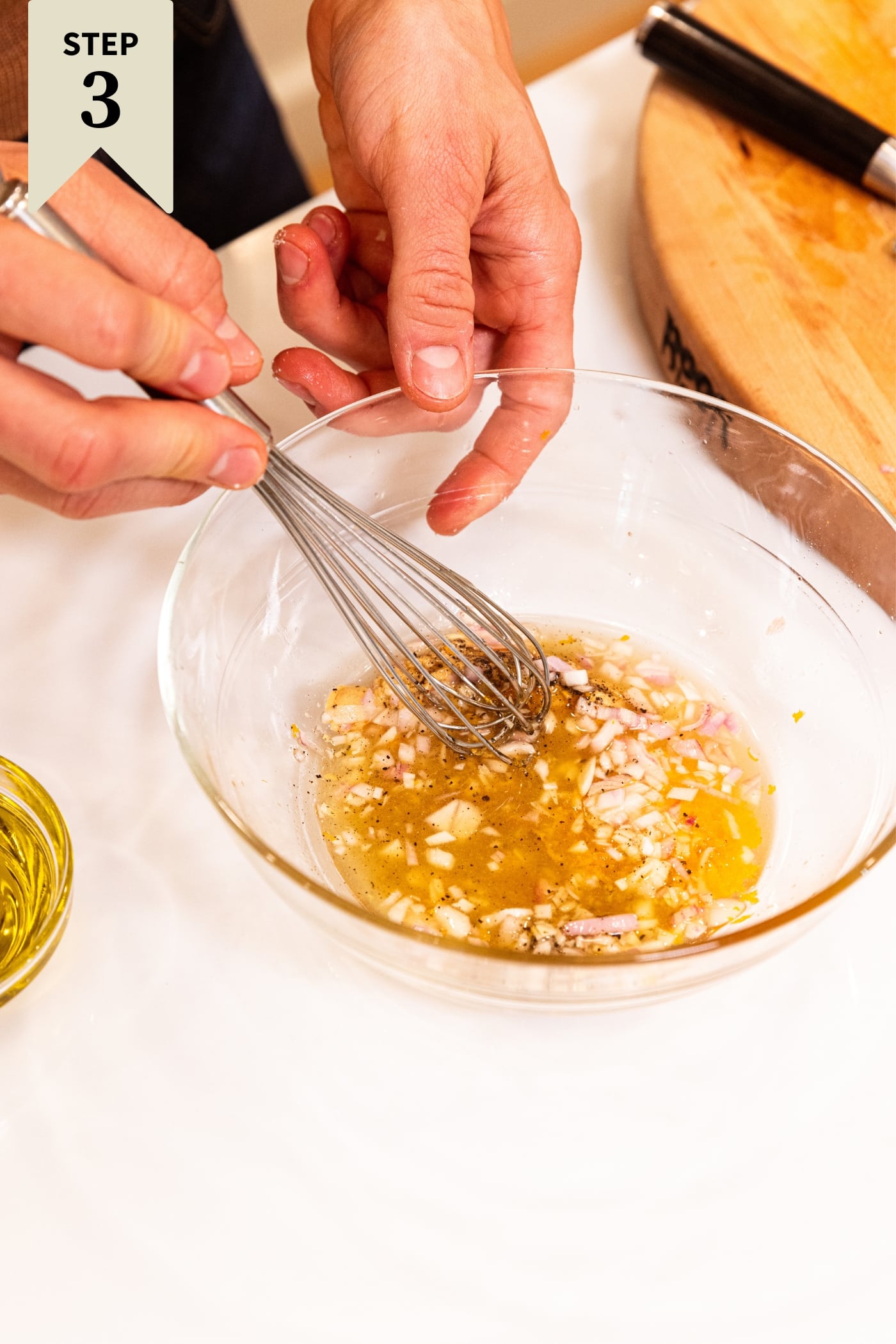 Small glass bowl filled with ingredients needed to make a homemade salad dressing with hand whisking all ingredients together all on white countertop.