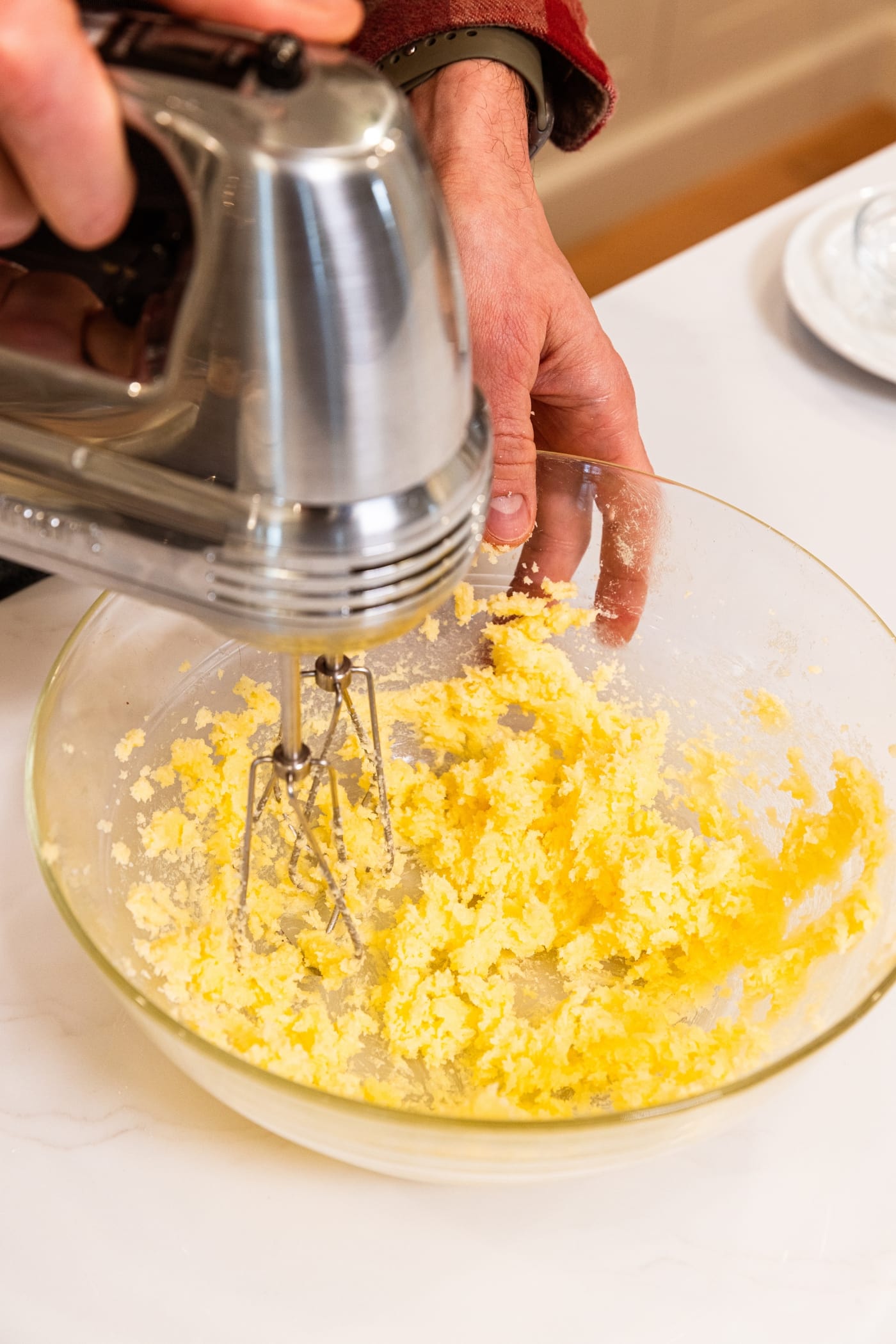 Glass mixing bowl with creamed butter and sugar mixture with hand mixer mixing everything together.
