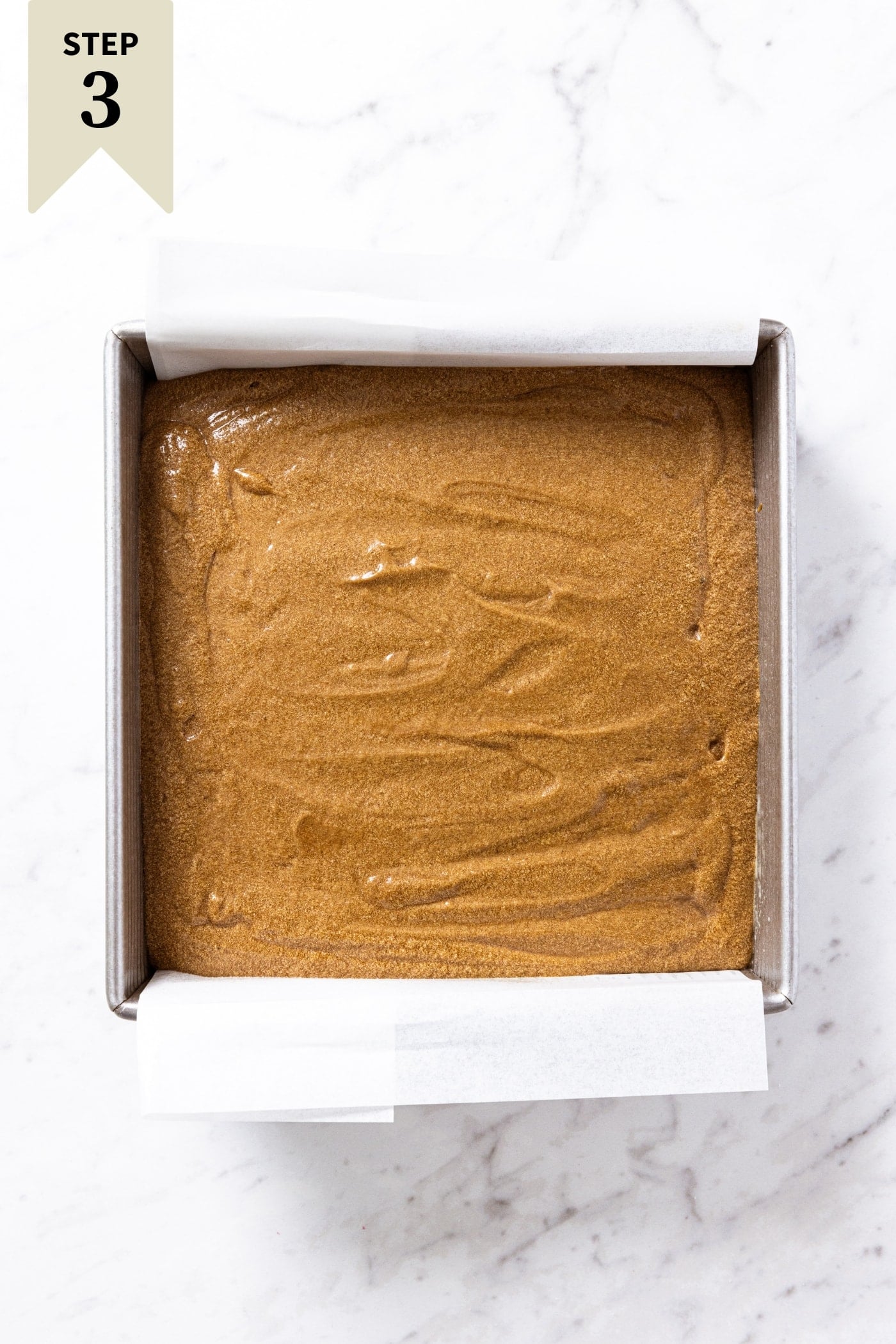 White marble surface with unbaked gingerbread spice cake with parchment underneath right before going into the oven.