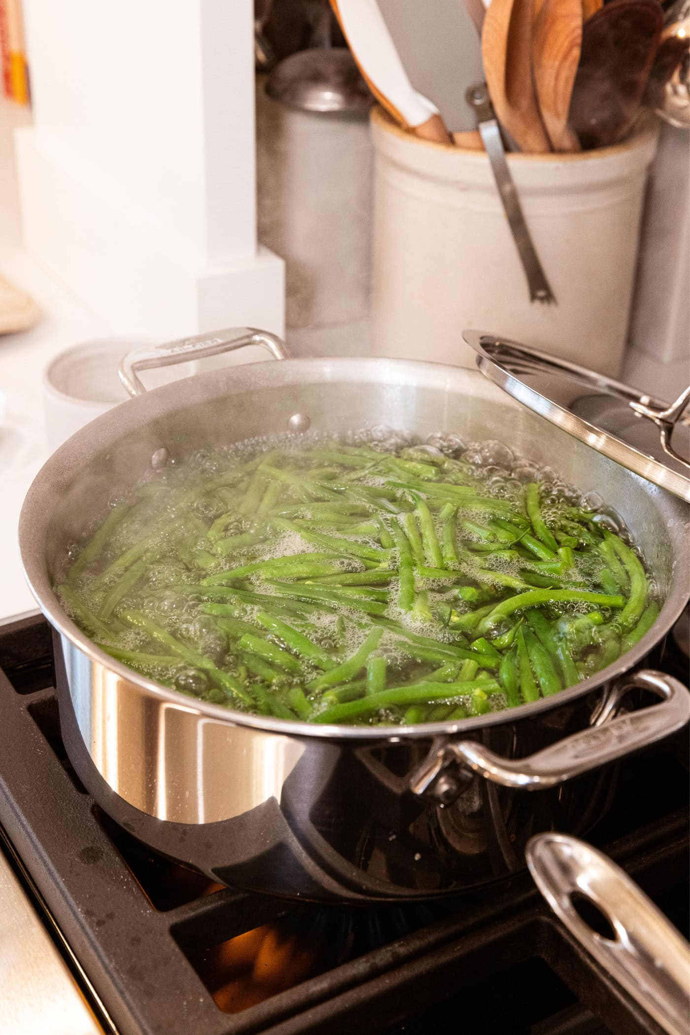 Stainless steel pot on the stovetop filled with blanching green beans in boiling water.