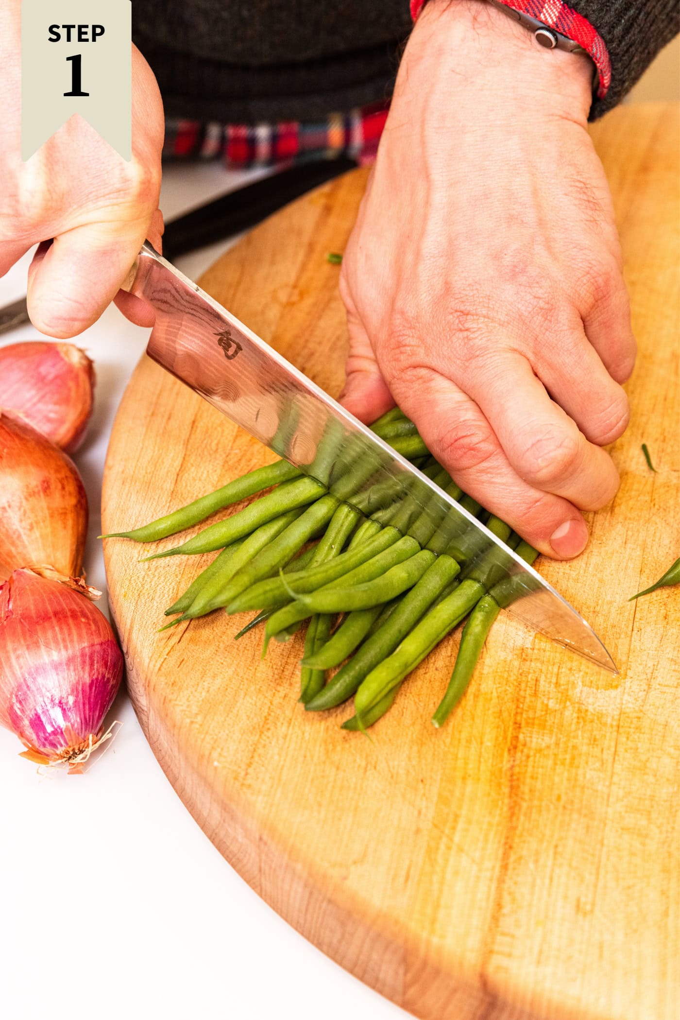 Hand using a knife to cut green beans in half for a green bean casserole.
