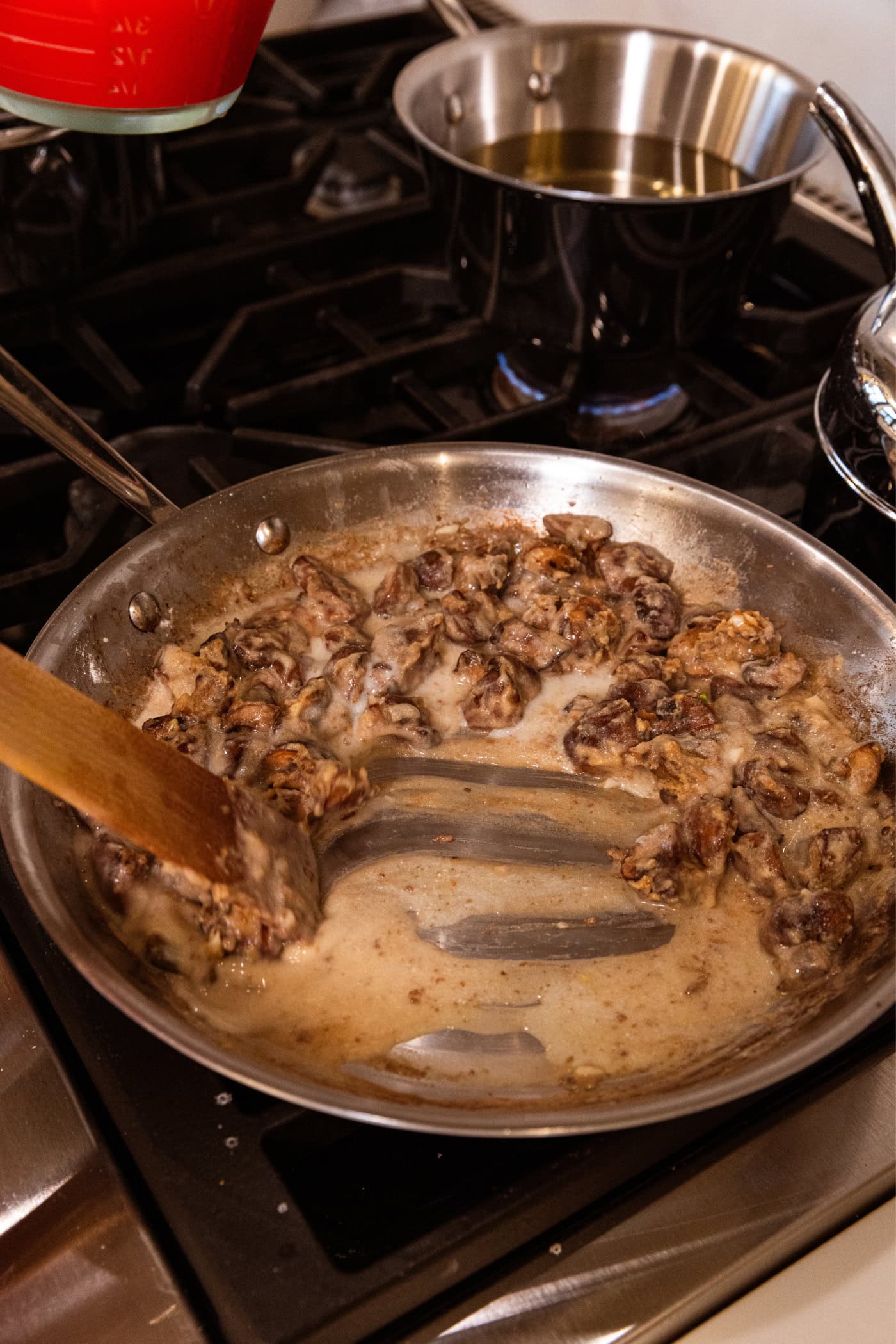 Wooden spatula stirring pieces of mushroom in a large stainless steel pan on the stovetop.