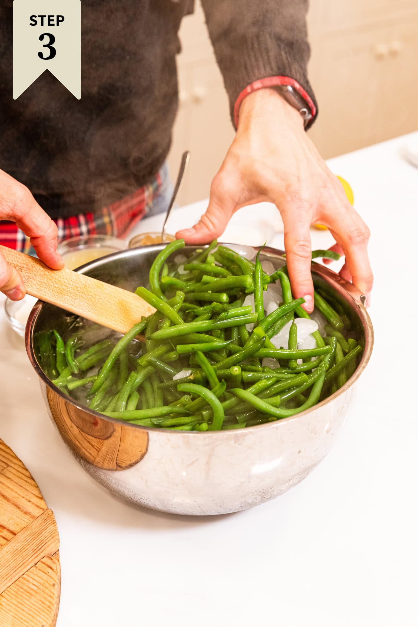 Green beans being placed in ice water bath in a stainless steel bowl to blanch.