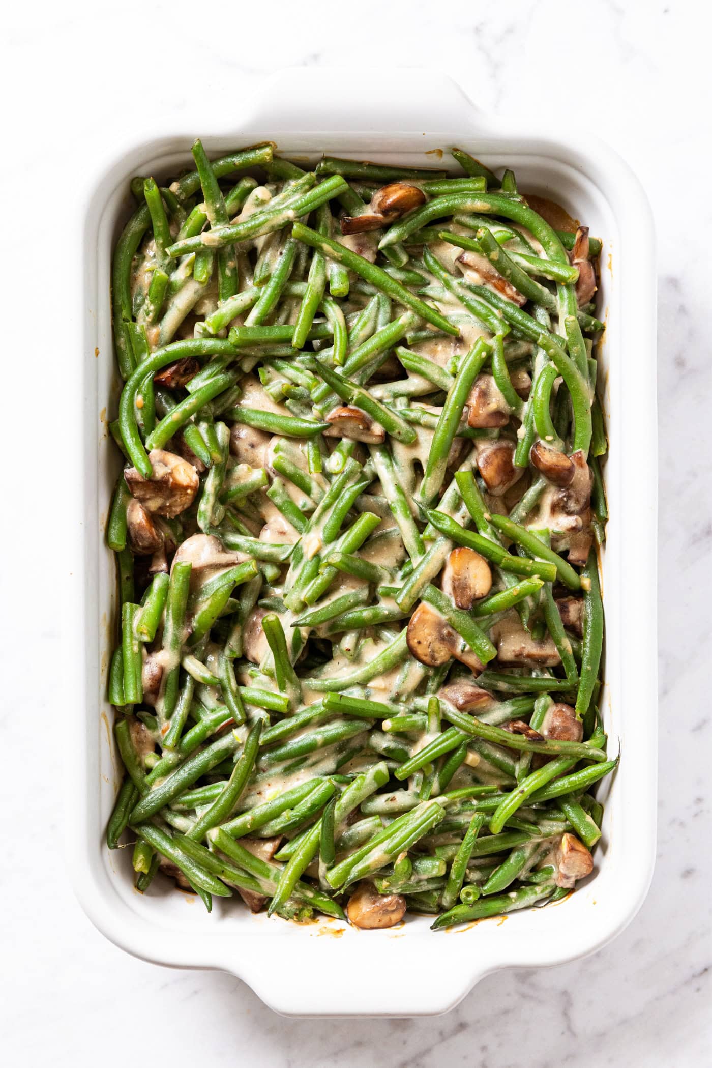 Green bean casserole with pieces of mushroom in a white baking dish right after coming out of the oven.
