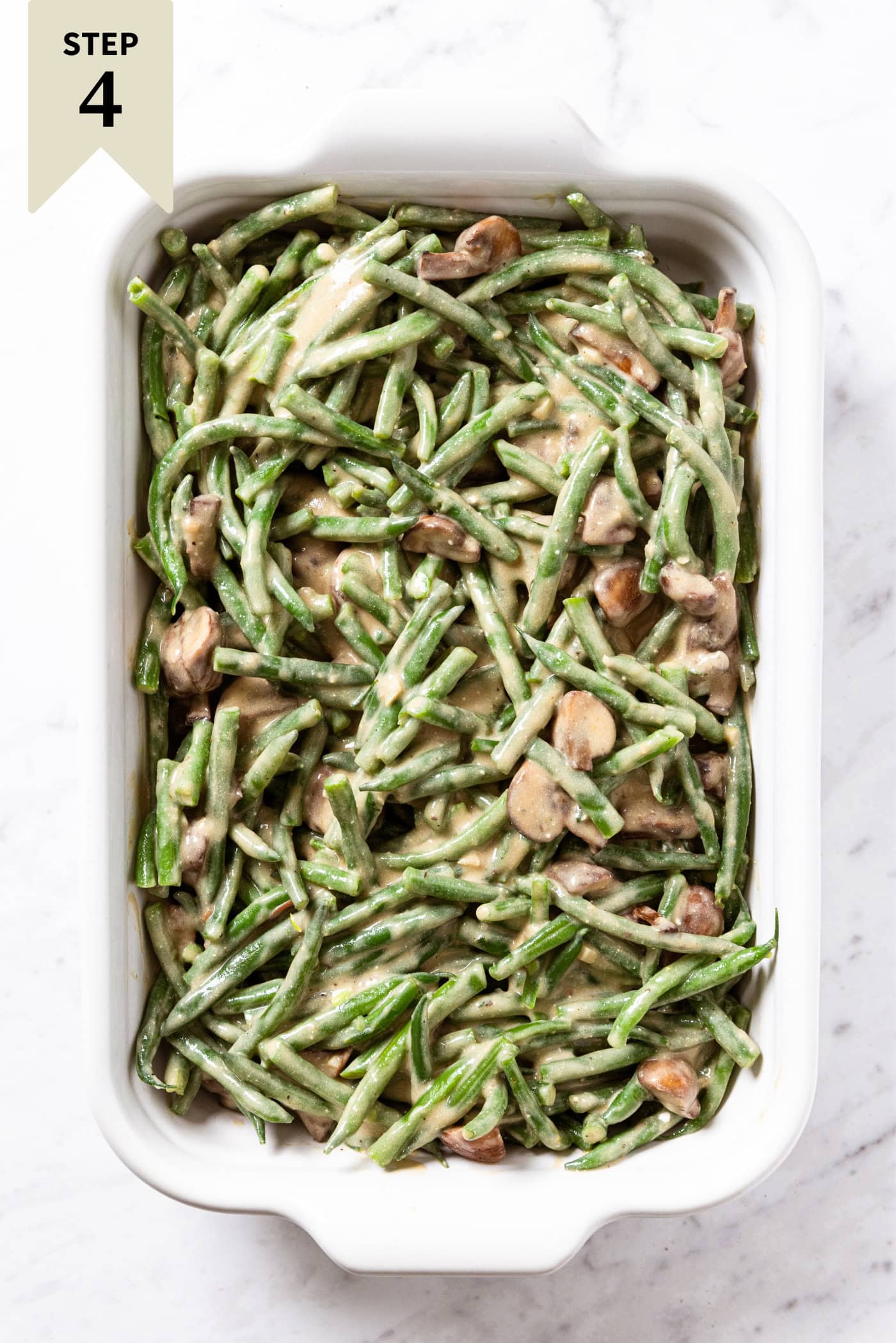 Unbaked green bean casserole in a white baking dish on a marble surface right before being baked.