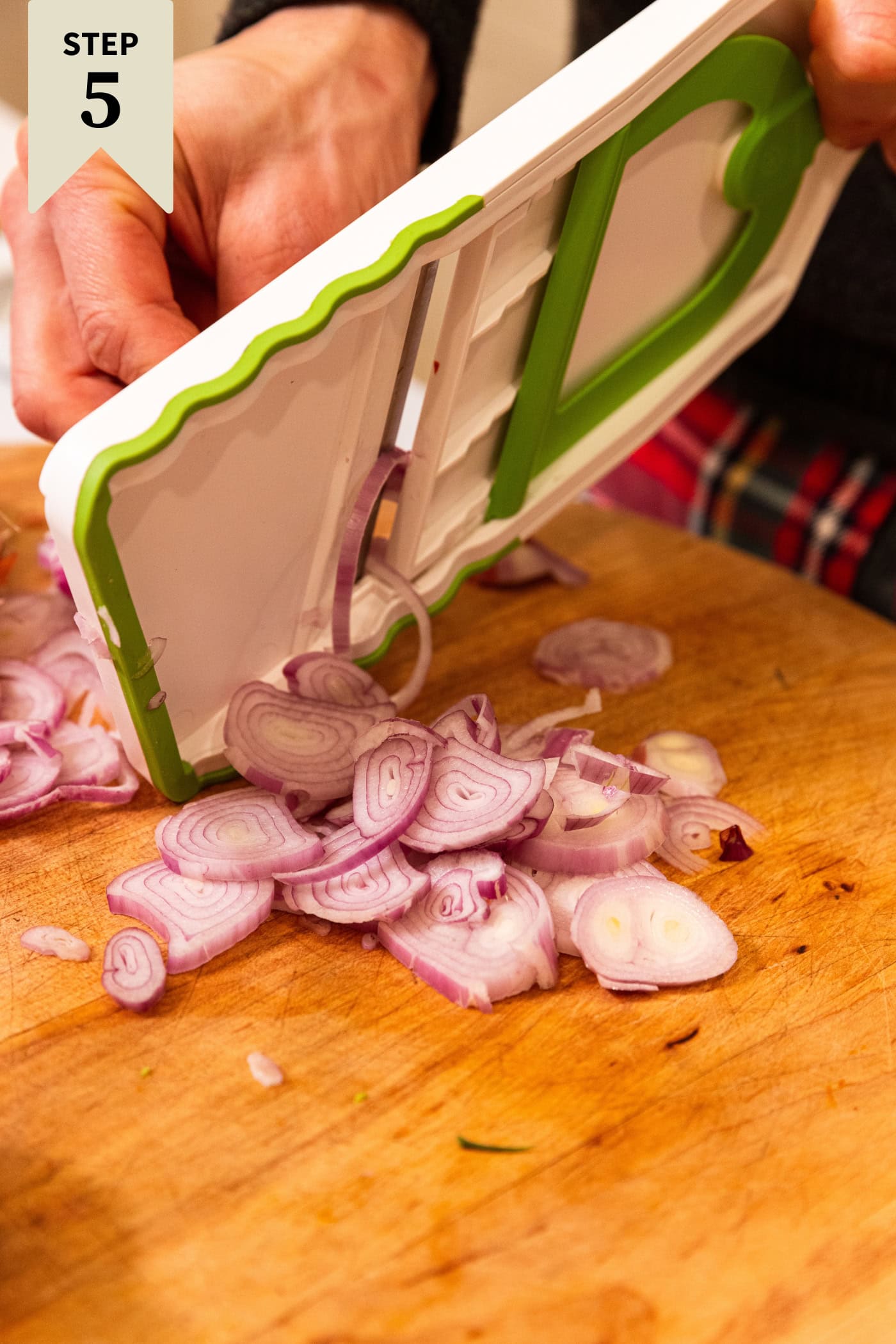 Mandolin slicing scallion into small pieces on a wooden cutting board.