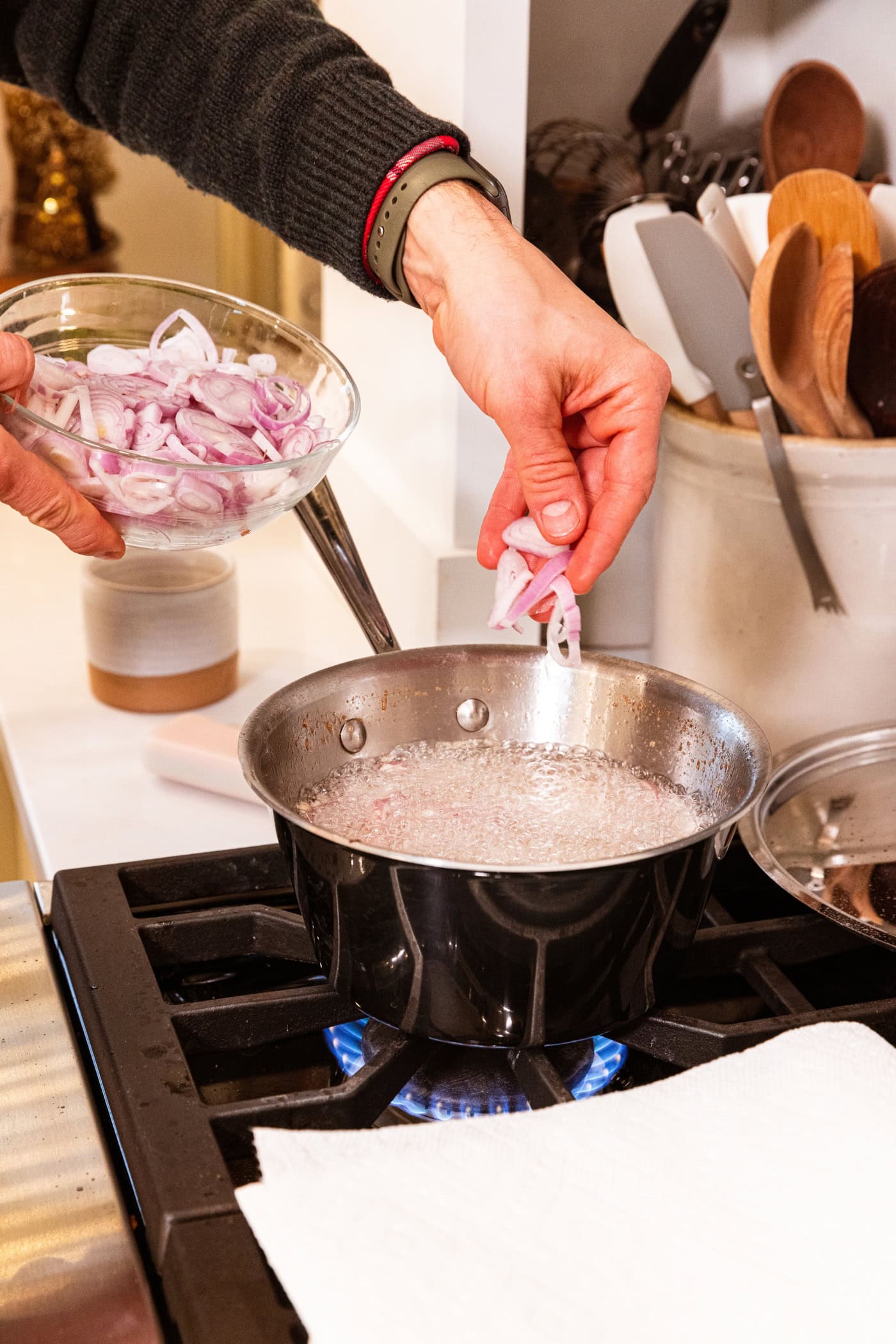 Hand placing raw uncooked scallion pieces into a boiling pot of oil on a stovetop.