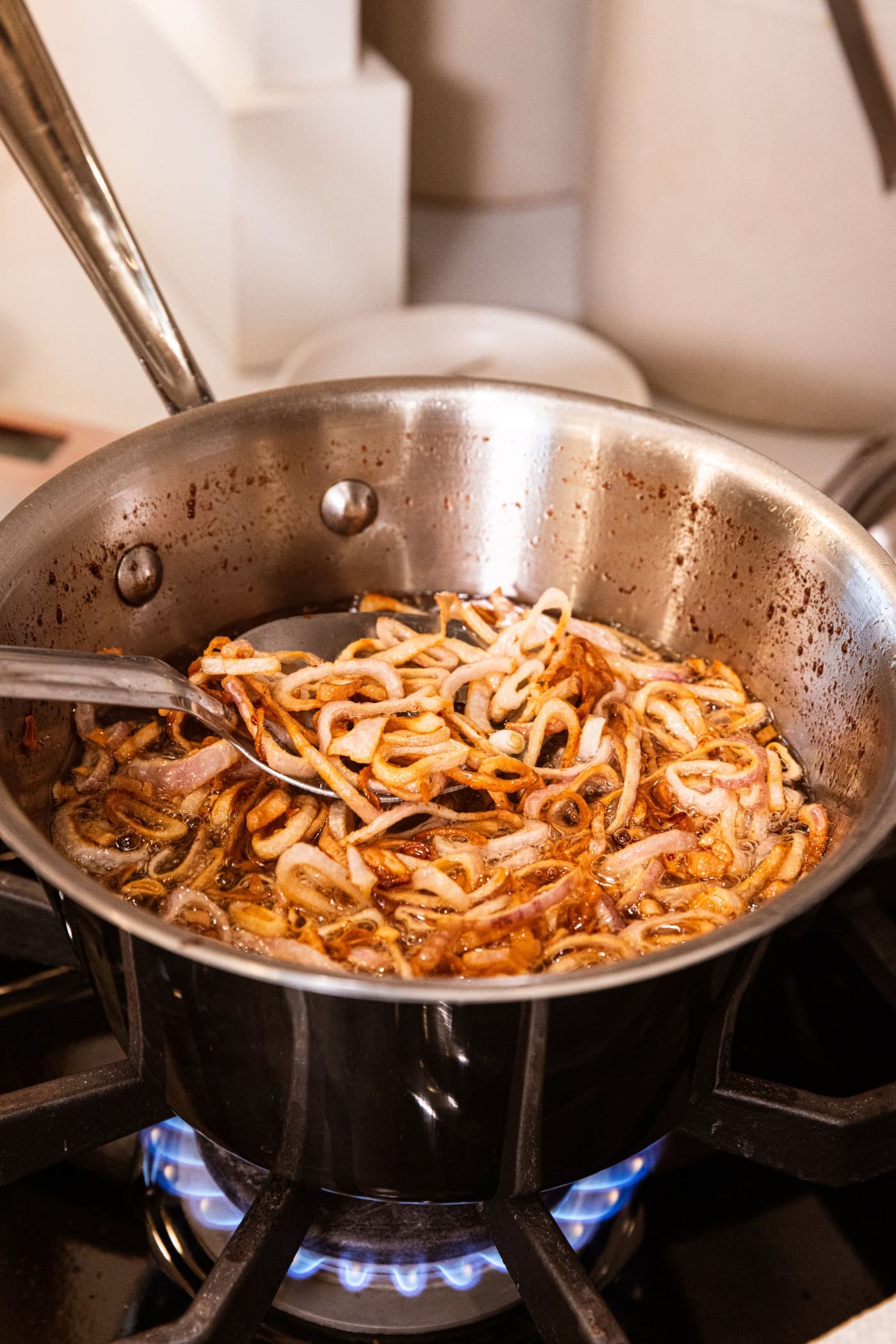Large stainless steel pan with crispy scallion pieces with spoon pulling some cooked pieces out.