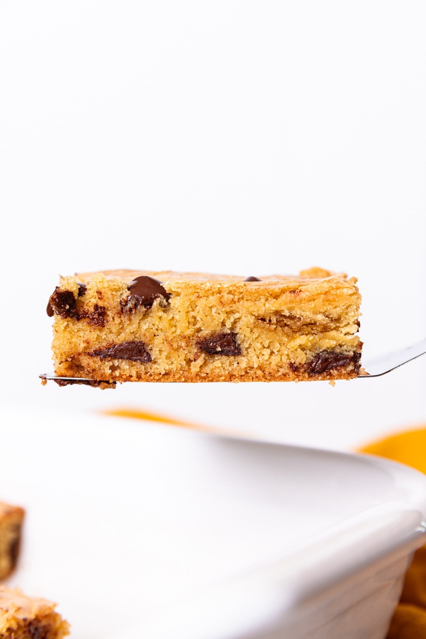 Side profile of baked blondie showing interior texture with chocolate chips dotted throughout with white background.