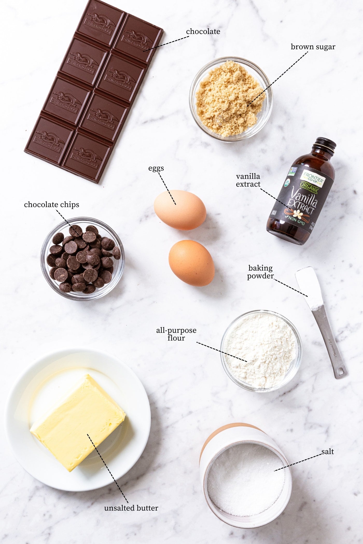 White marble surface filled with all ingredients needed to make blondies including flour, butter, eggs, brown sugar, chocolate, and more.