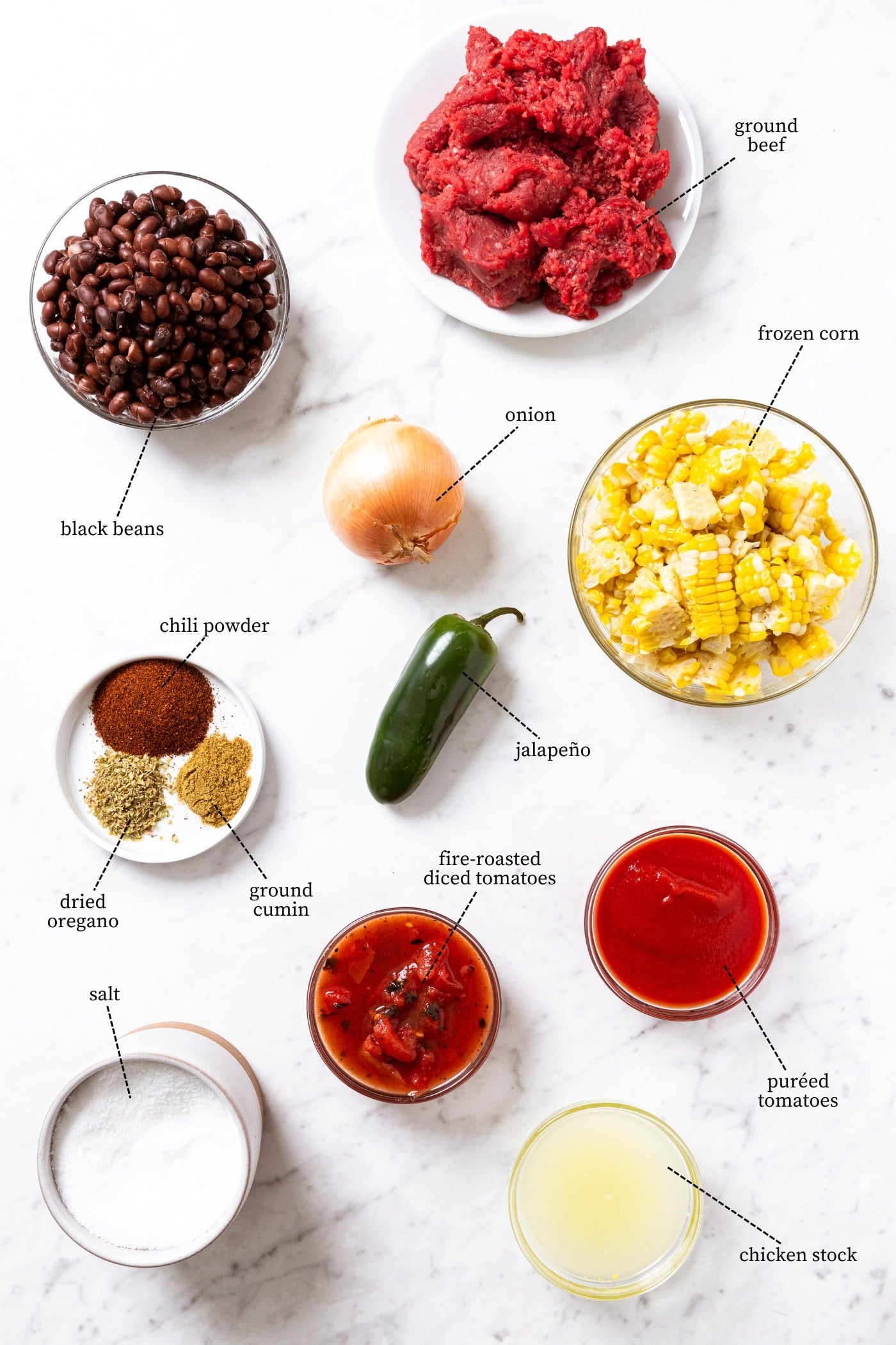 White marble surface filled with all ingredients needed to make taco soup including ground beef, black beans, frozen corn, tomatoes, spices, and more.