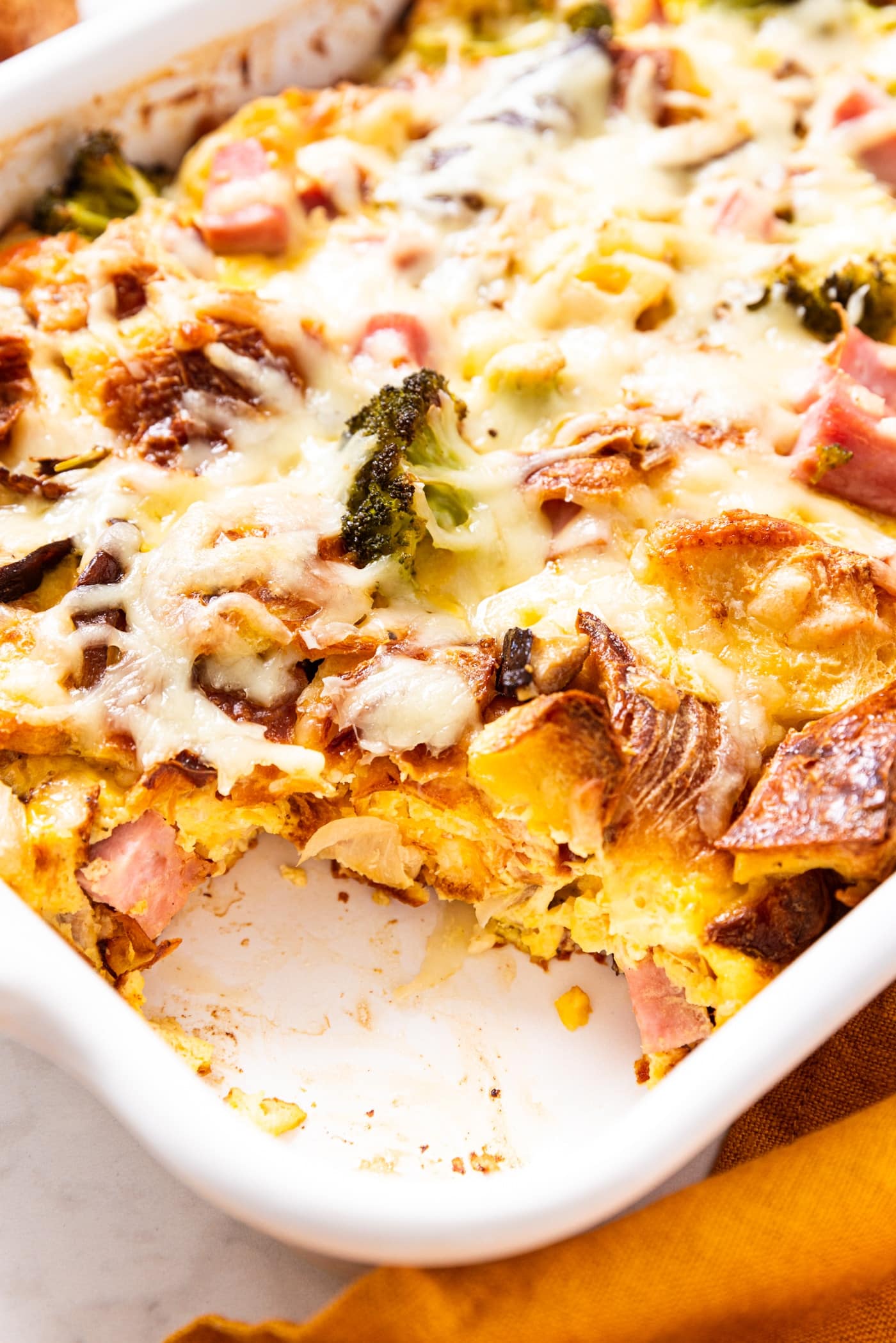 White baking dish filled with egg casserole with scoop taken out showing egg interior of casserole.