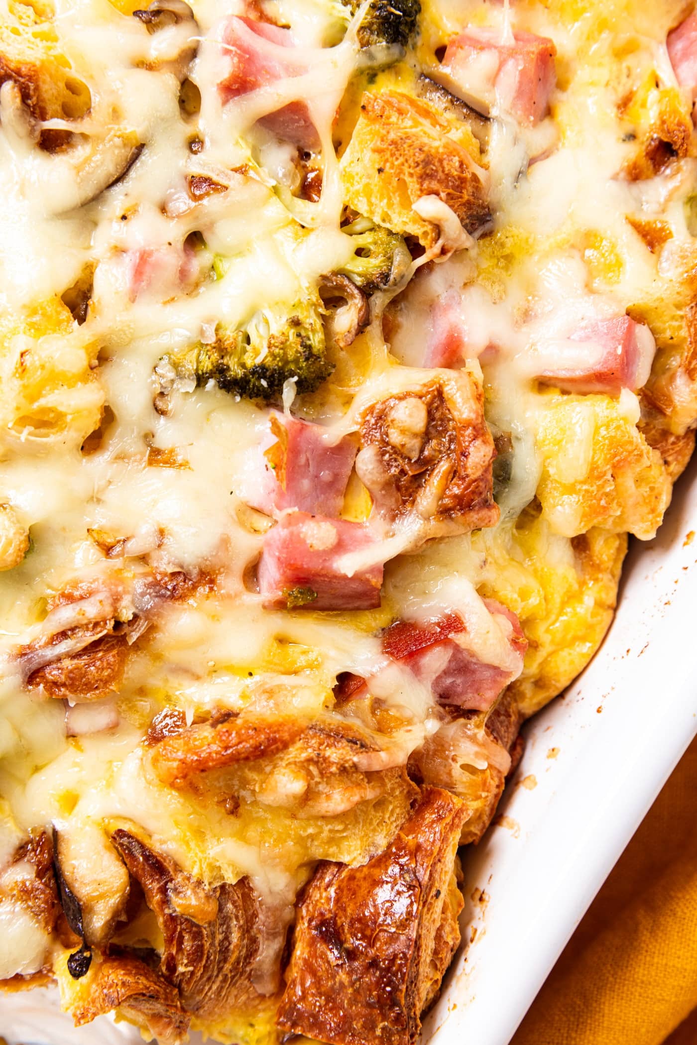 White baking dish filled with baked ham and cheese egg casserole with melted cheese all over the top with broccoli and ham peeking out.