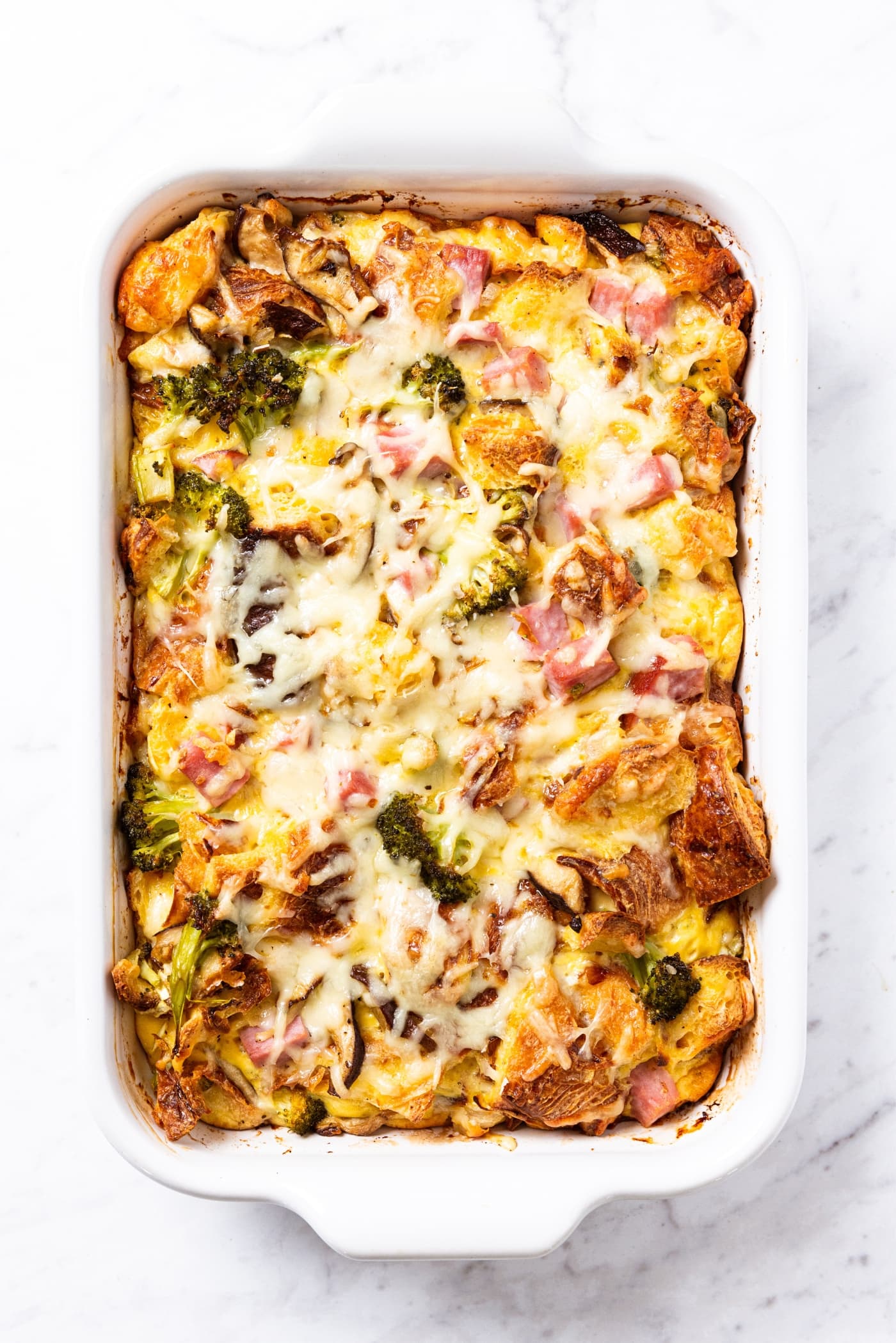 White marble surface with white baking dish filled with egg casserole after coming out of the oven after being baked with melted cheese all over the top.
