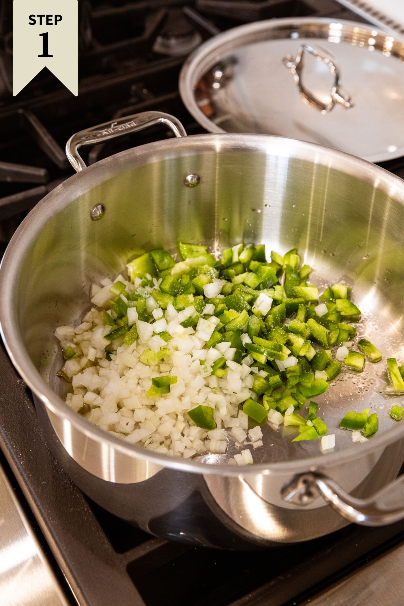 Metal stockpot filled with diced green bell pepper and onion sautéing in butter on stovetop.