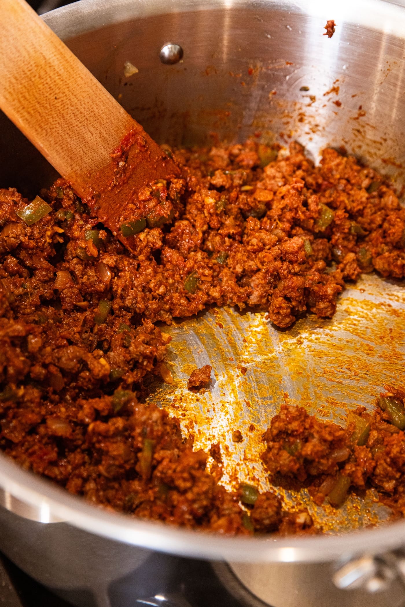 Wooden spatula mixing around browned beef mixed with tomato paste showing slight brown film on bottom of stockpot.