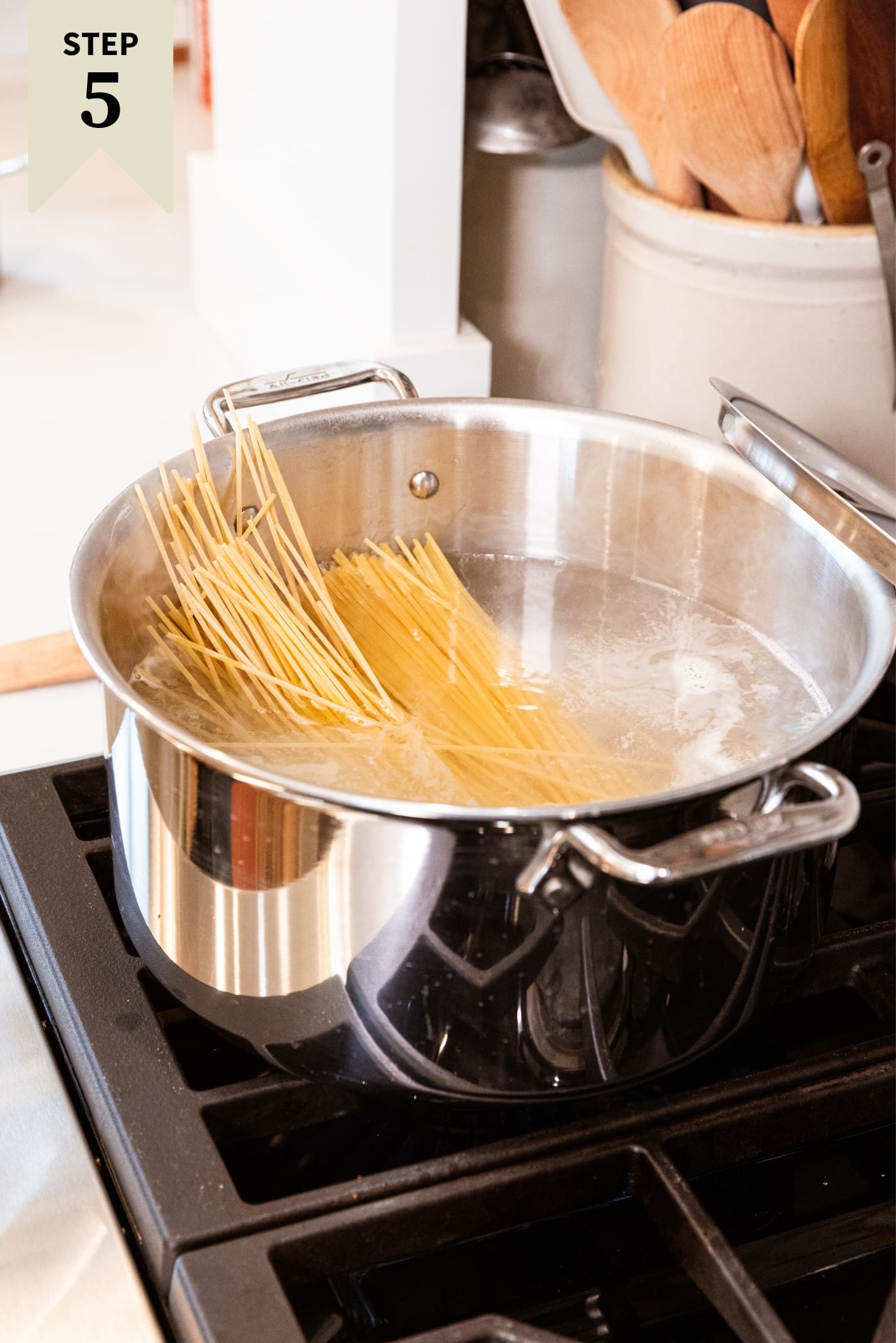 Large metal stockpot sitting on stovetop filled with water and uncooked spaghetti leaning against the side of the stockpot.