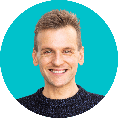 Kaleb Wyse standing in front of bright blue background wearing dark navy sweater.