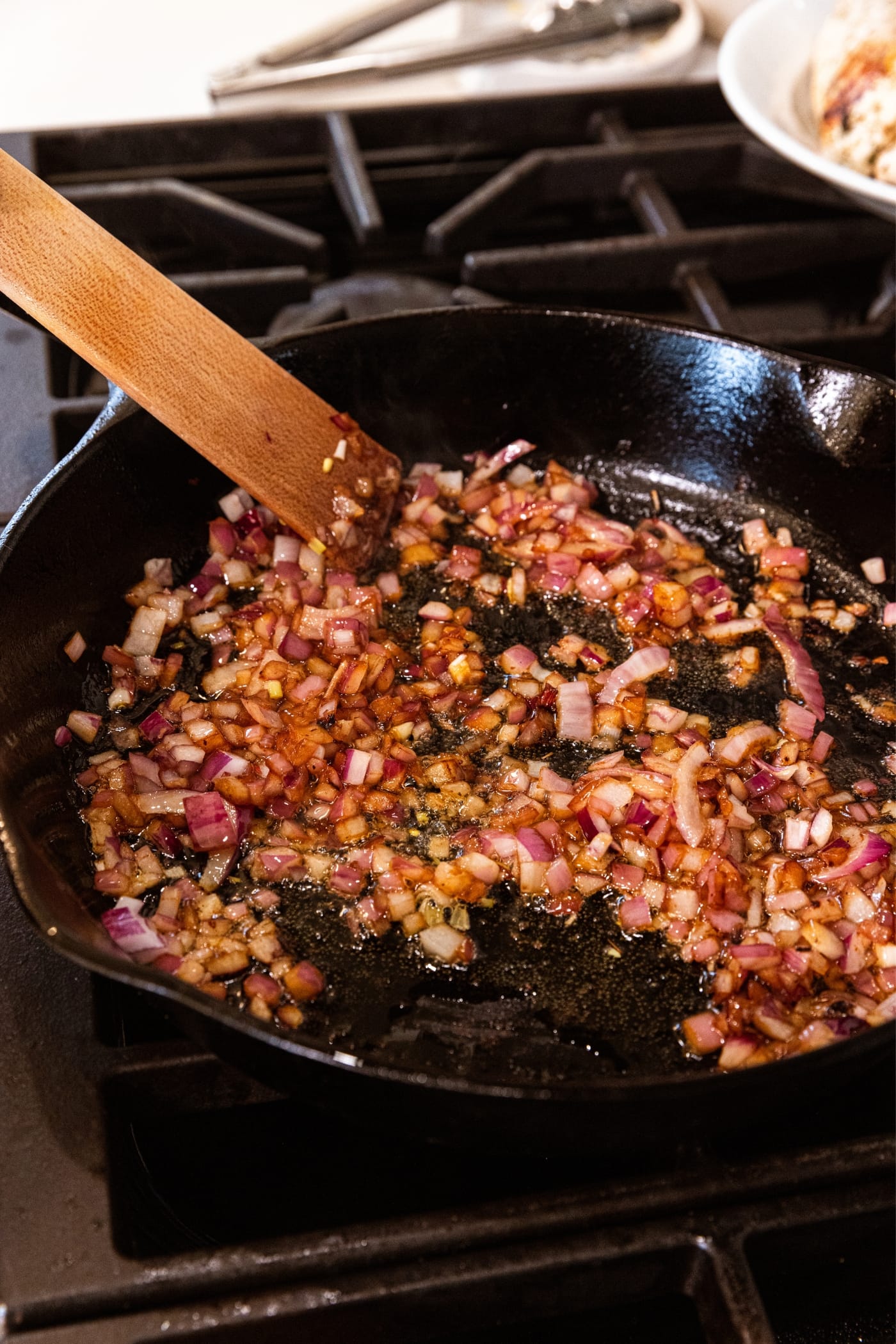 Wooden spatula mixing around browned red onion in black cast iron skillet on stovetop.