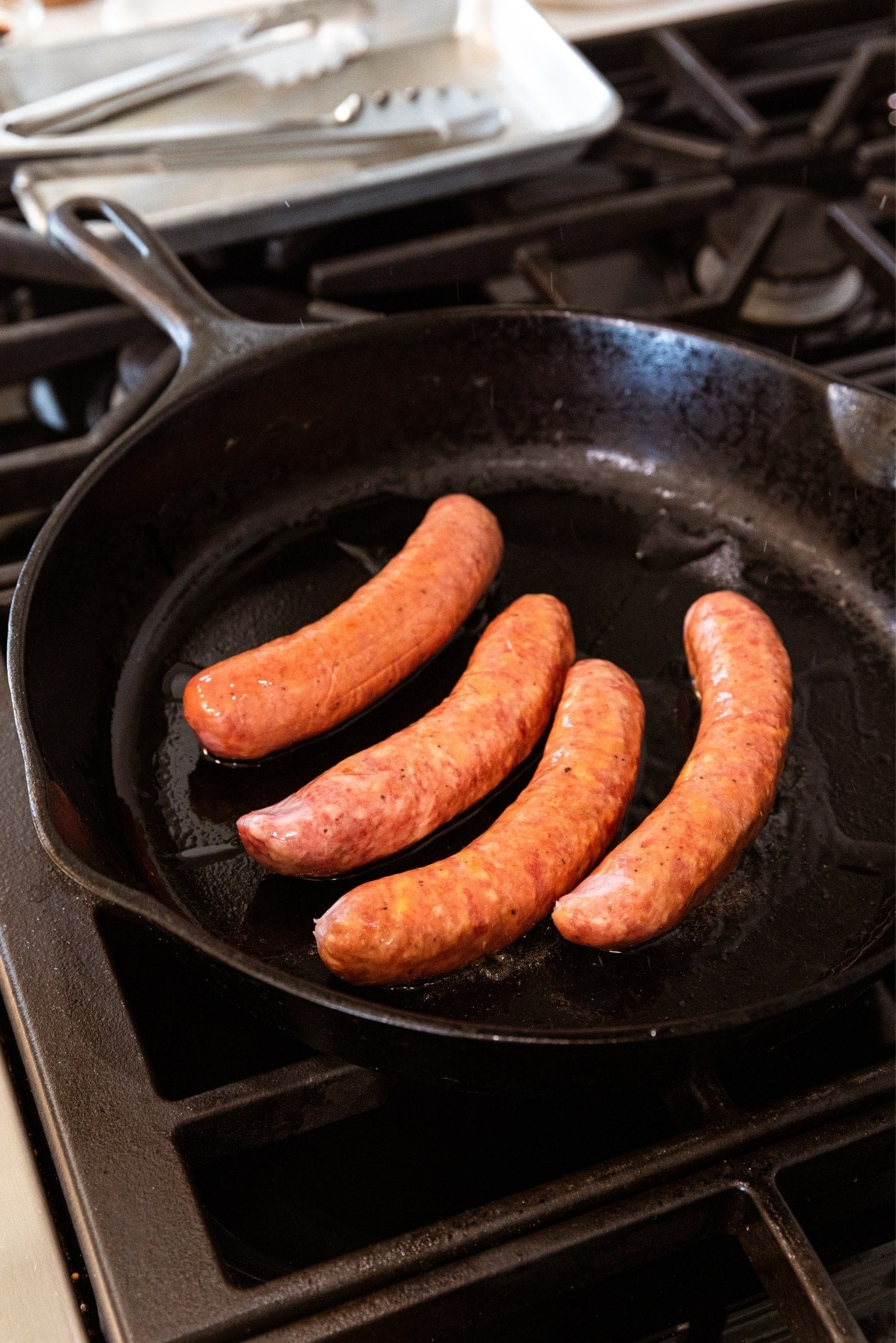 Four links of sausage in a black skillet on stovetop before being browned.