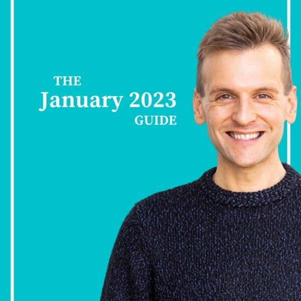 Kaleb Wyse wearing a dark navy blue sweater standing in front of bright blue background smiling.