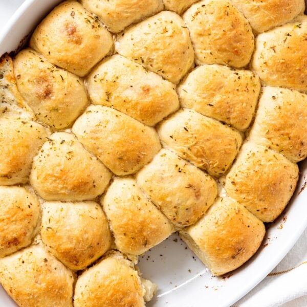 White oval baking dish filled with small pizza bites with one missing showing golden tops of dough all on white marble surface.