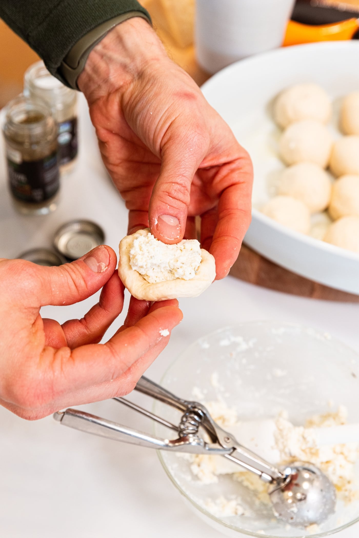 Hands forming pizza bite with scoop of ricotta cheese mixture sitting on the dough before being squeezed together.