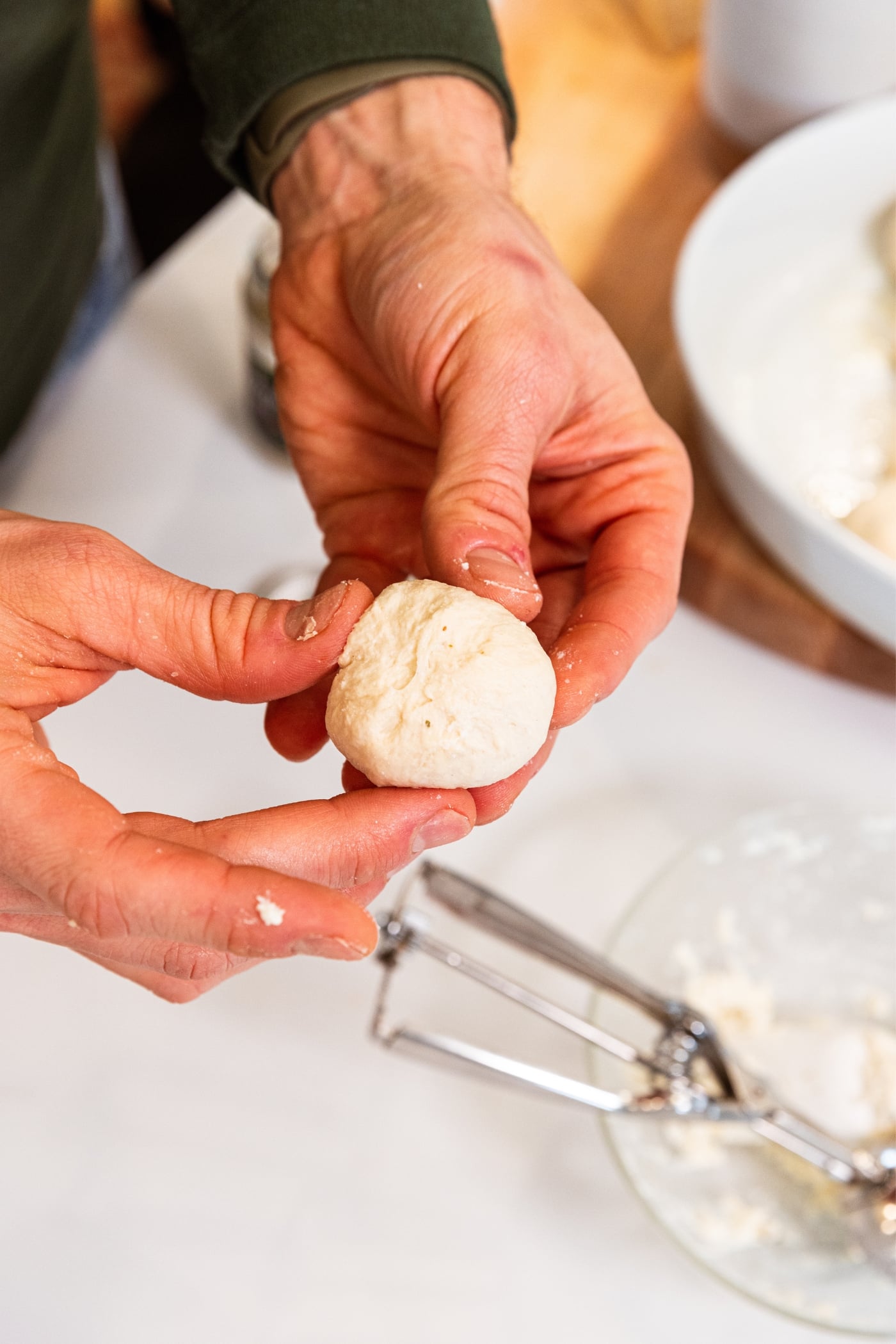 Hand pressing together sides of dough ball to form a pizza bite with ricotta cheese mixture inside.