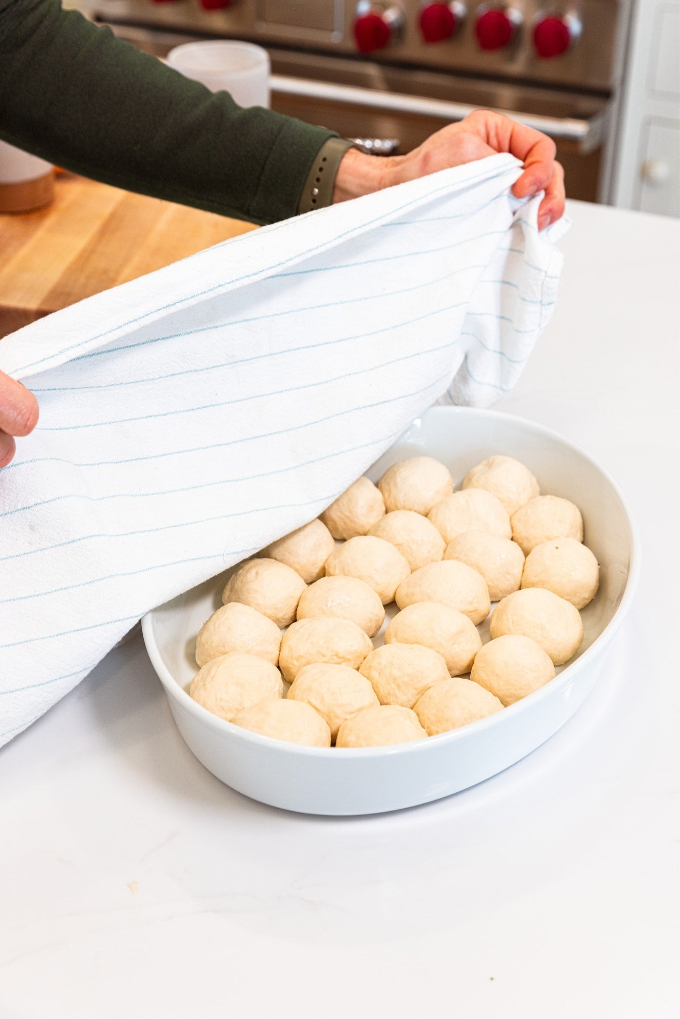 Hands placing towel over the top of an oval white baking dish filled with pizza bites right before rising again.