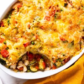 White oval baking dish filled with baked spaghetti squash chicken casserole on white marble surface with melted cheese over the top.