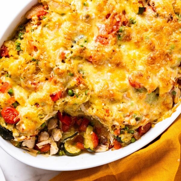 White oval baking dish filled with baked spaghetti squash chicken casserole on white marble surface with melted cheese over the top.